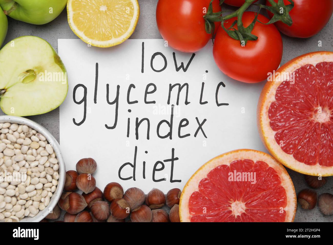 Paper with words Low Glycemic Index Diet and food on grey table, flat lay Stock Photo
