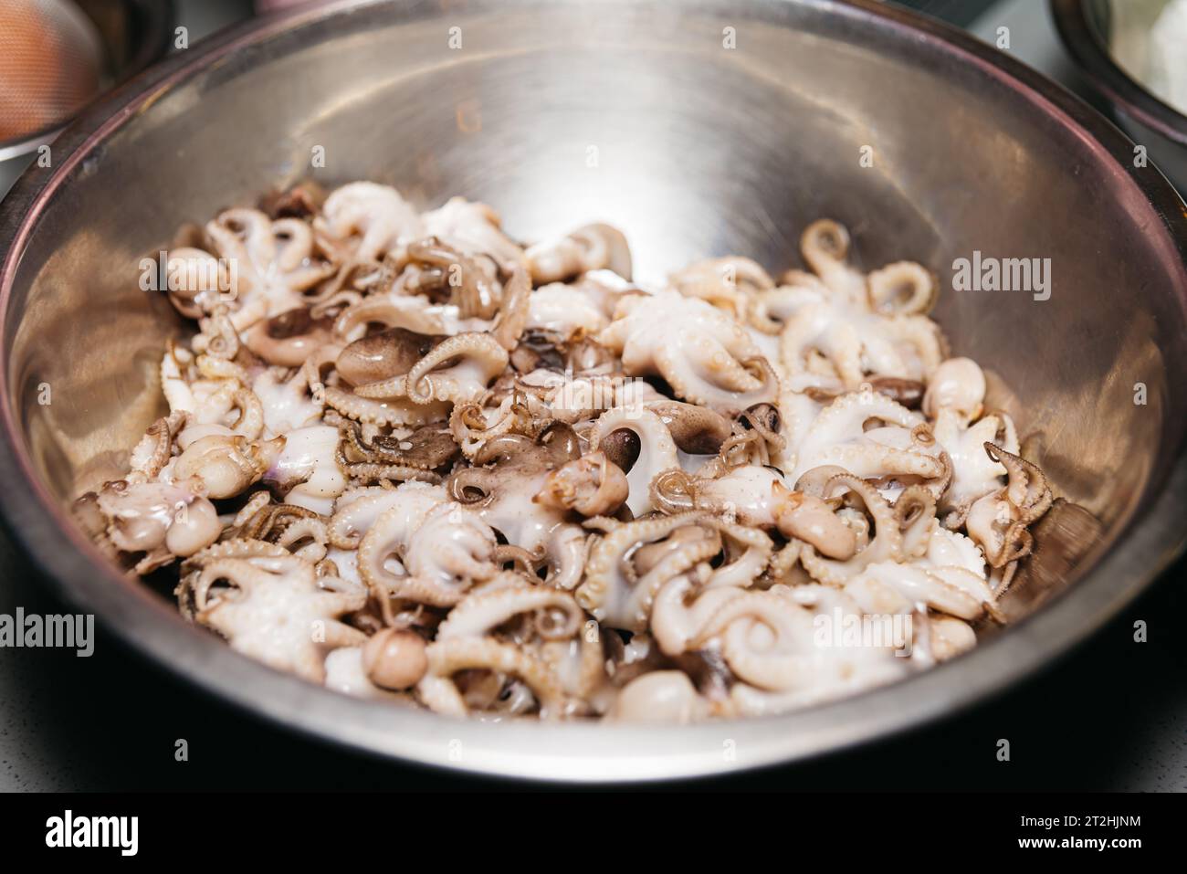 Small raw octopuses in a bowl. Defrosted thawed cephalopods. Close-up. Selective focus. Stock Photo