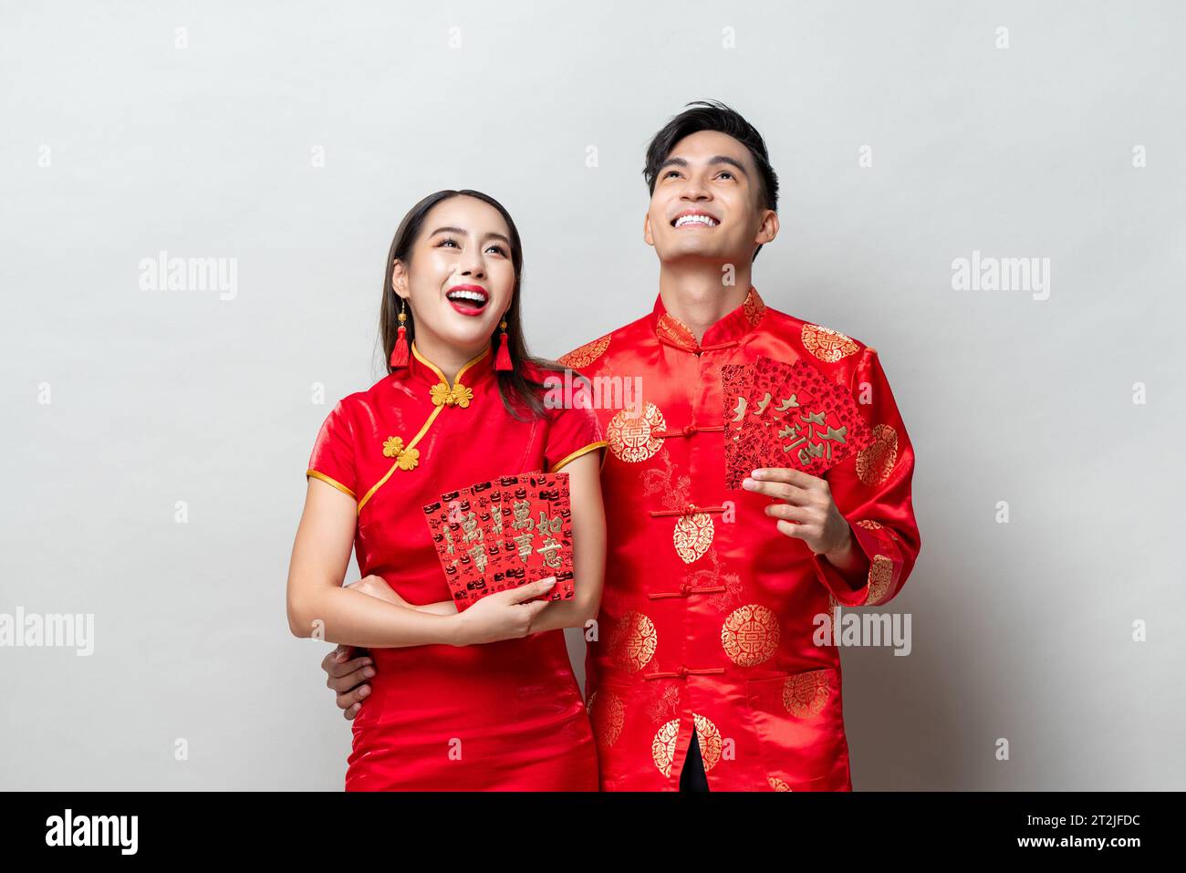 Asian couple in traditional oriental costumes holding red envelopes or Ang Pow in gray background for Chinese new year concepts, foreign texts mean gr Stock Photo