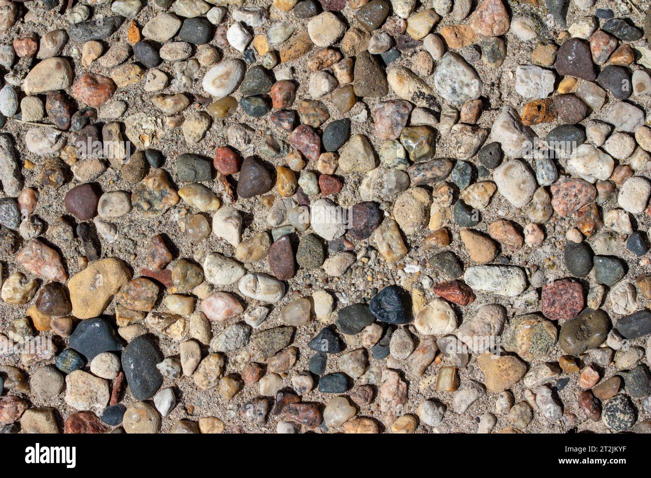 Full frame abstract macro texture background of an old aggregate walking surface with exposed stones and pebbles in bright sunlight Stock Photo
