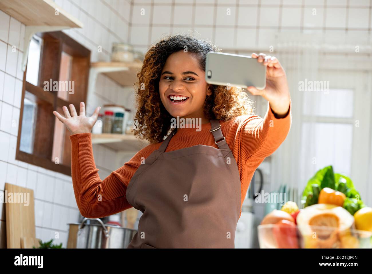 Happy African American lady using cellphone during online class in blurred background of the kitchen Stock Photo