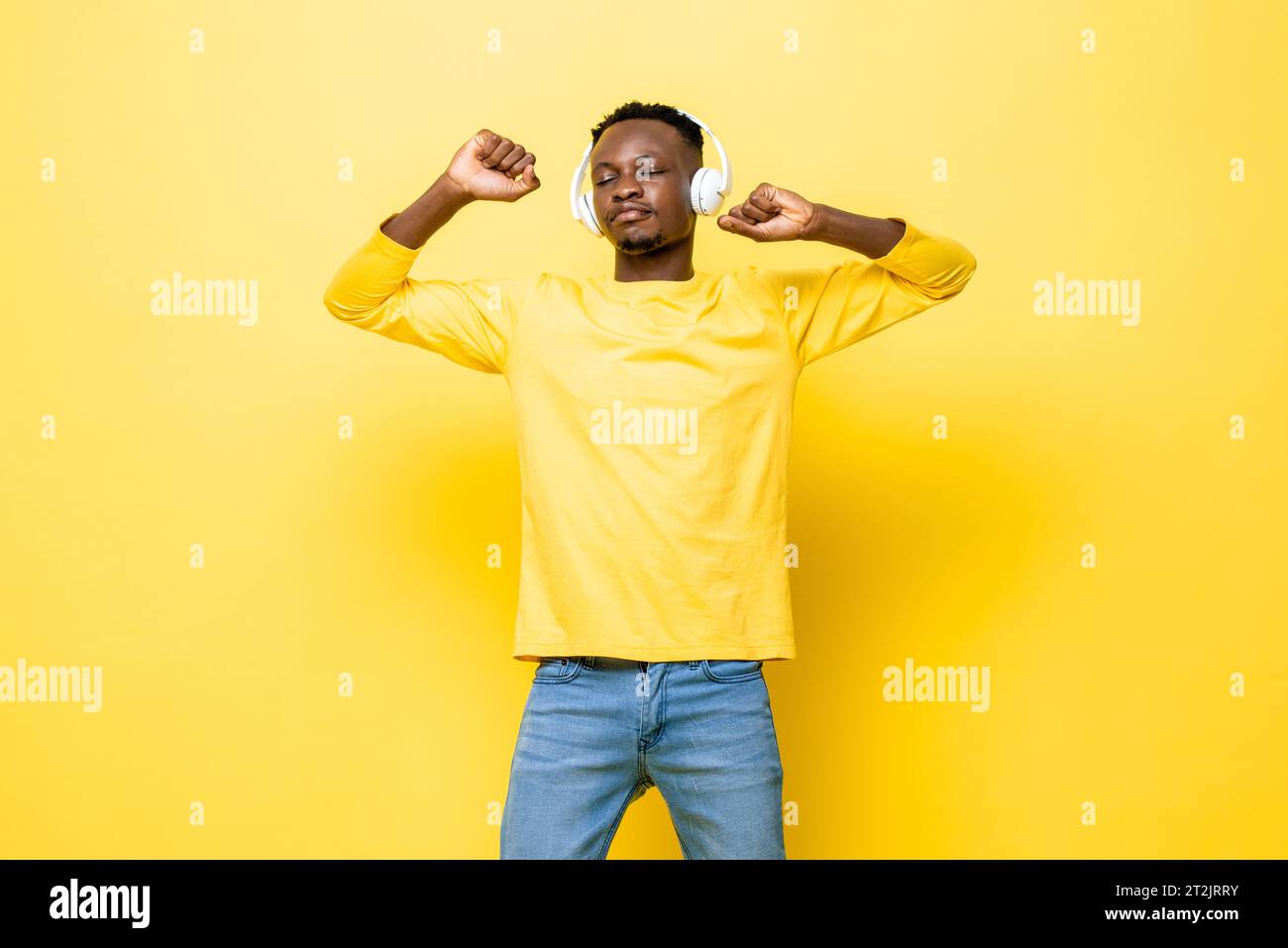 Portrait of young African man listening to music on headphones closing eyes and dancing against yellow studio background Stock Photo