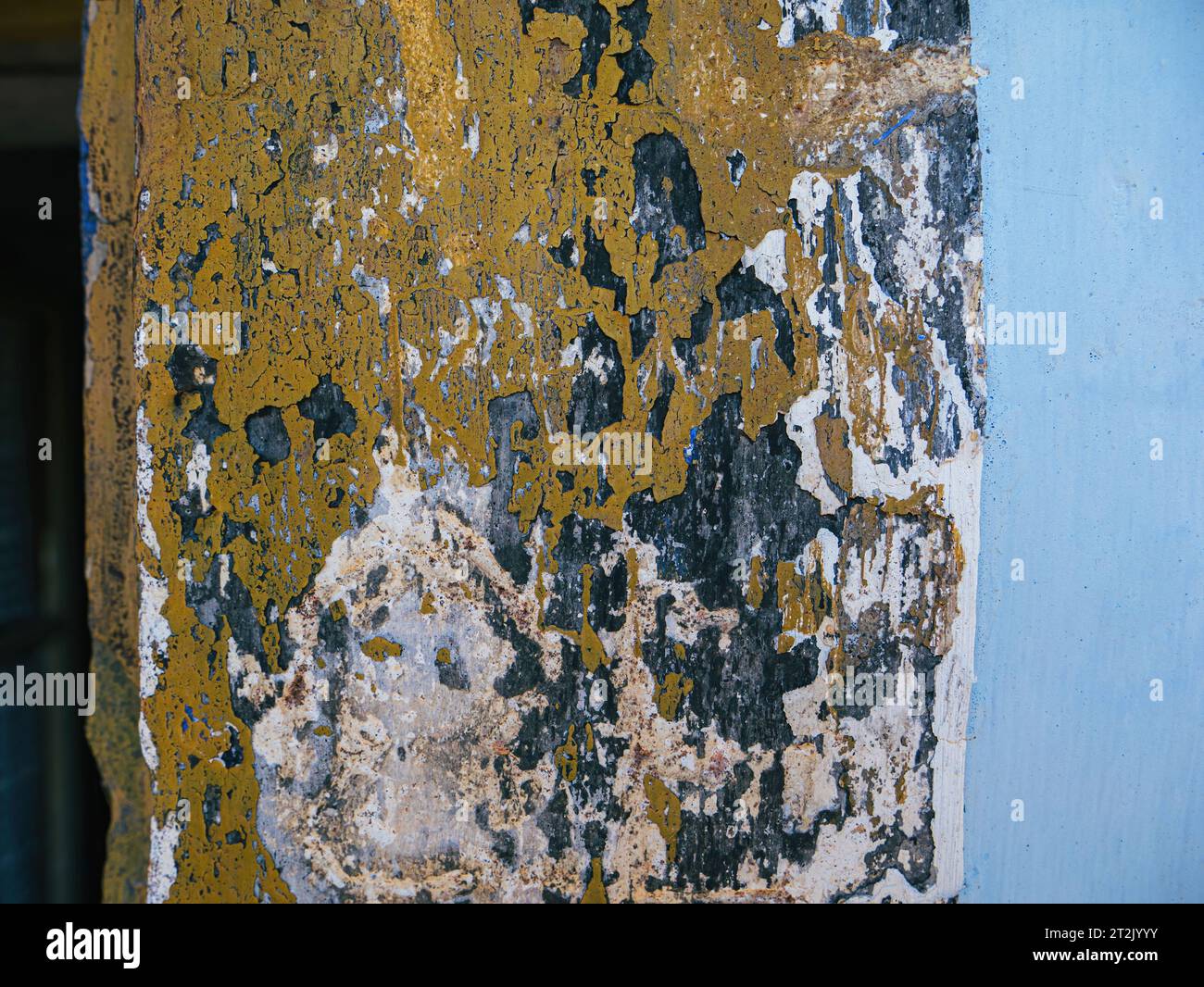 The window sill of an aged house bears the traces of time, revealing multiple layers of paint, transitioning from a deep blue hue to a warm, sunlit yellow on the weathered facade Stock Photo