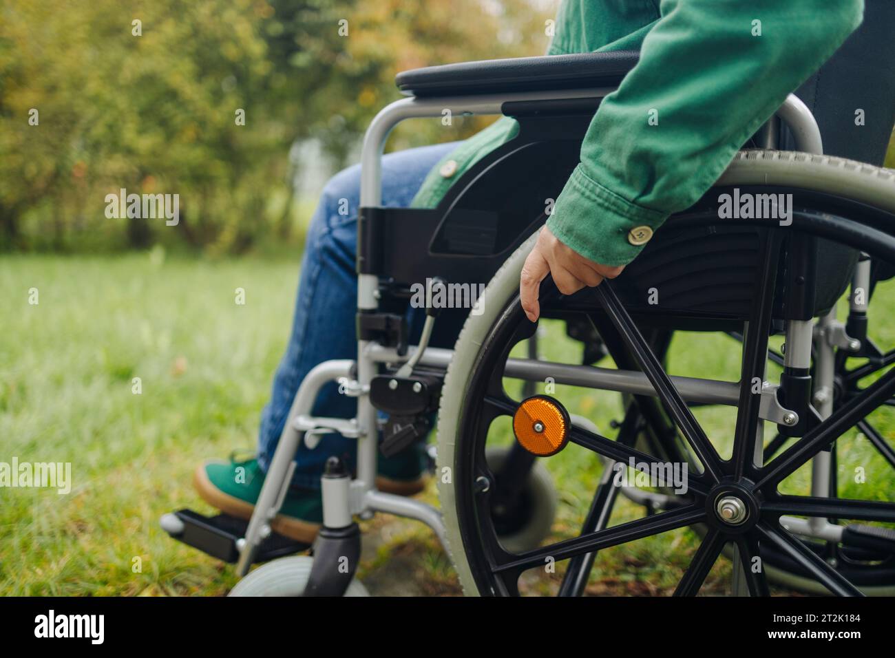 Close-up of female hand on wheel of wheelchair during walk in park ...