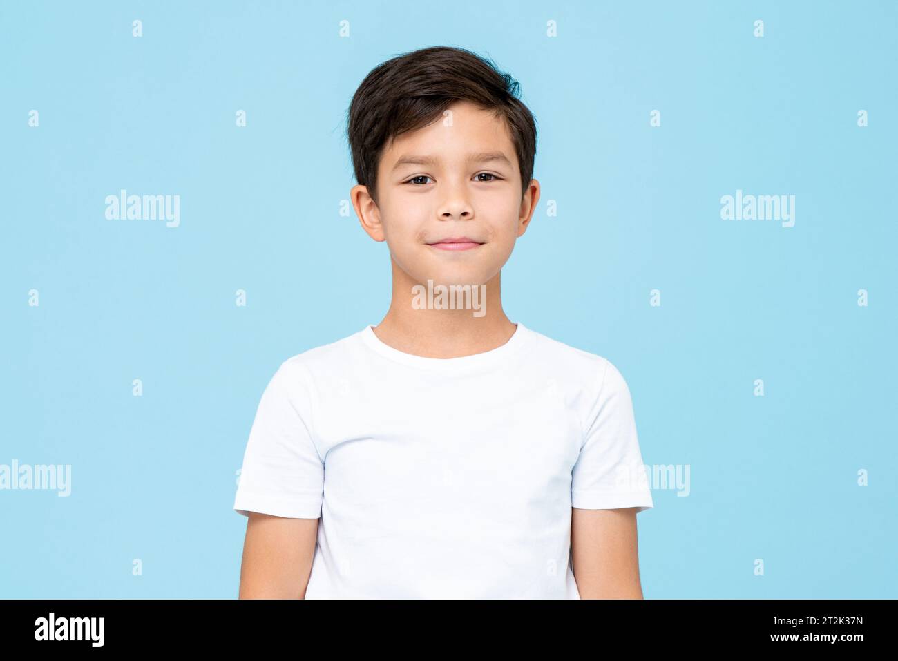 Cute smiling boy in plain white t shirt looking at camera in isolated studio light blue color