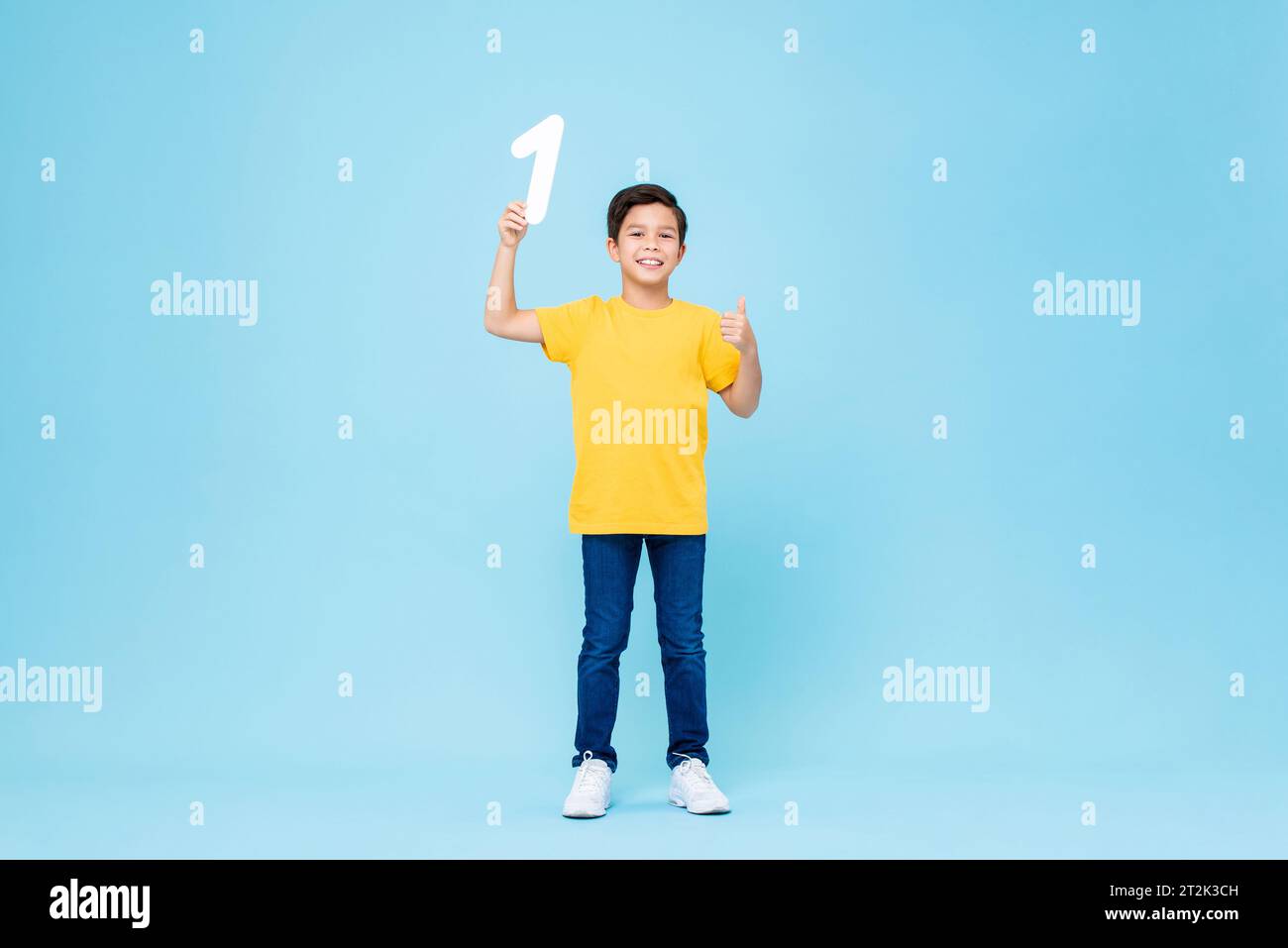 Cute mixed race boy giving thumbs up and holding number one in isolated light blue studio background Stock Photo