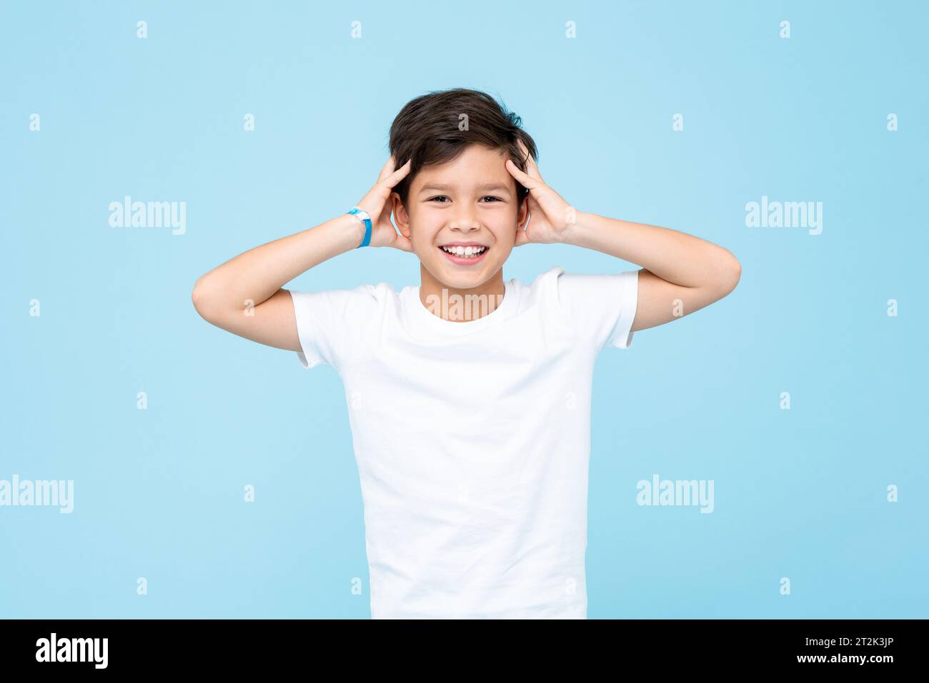 Cute boy in plain white t shirt smiling and touching head in studio light blue isolated color background Stock Photo