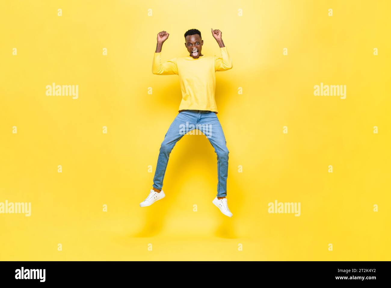 Surprised excited African man jumping with hands raised in studio yellow color isolated background Stock Photo