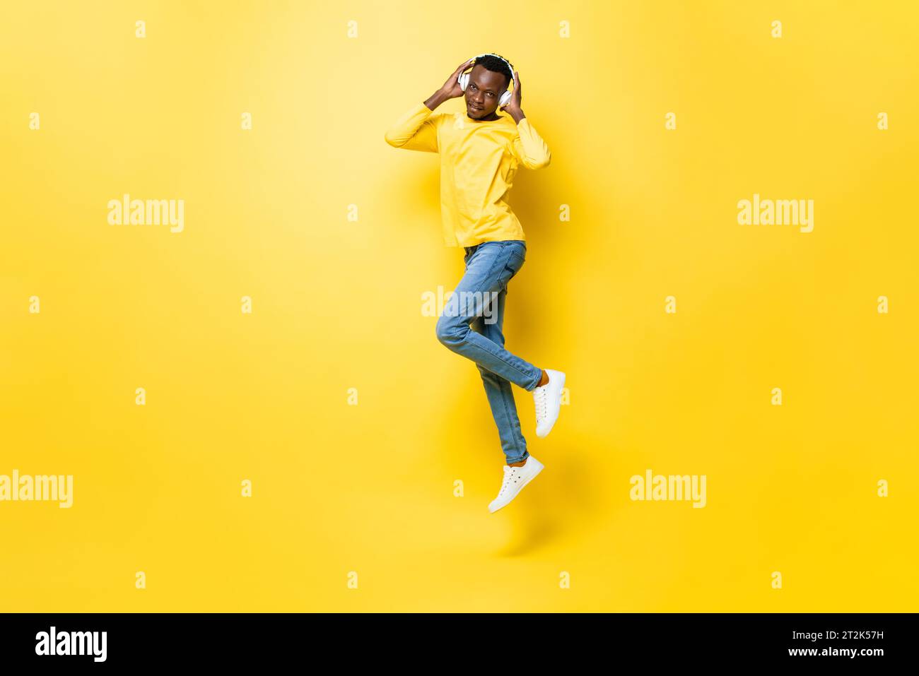 Young African man listening to music on headphones and jumping in isolated yellow studio background Stock Photo