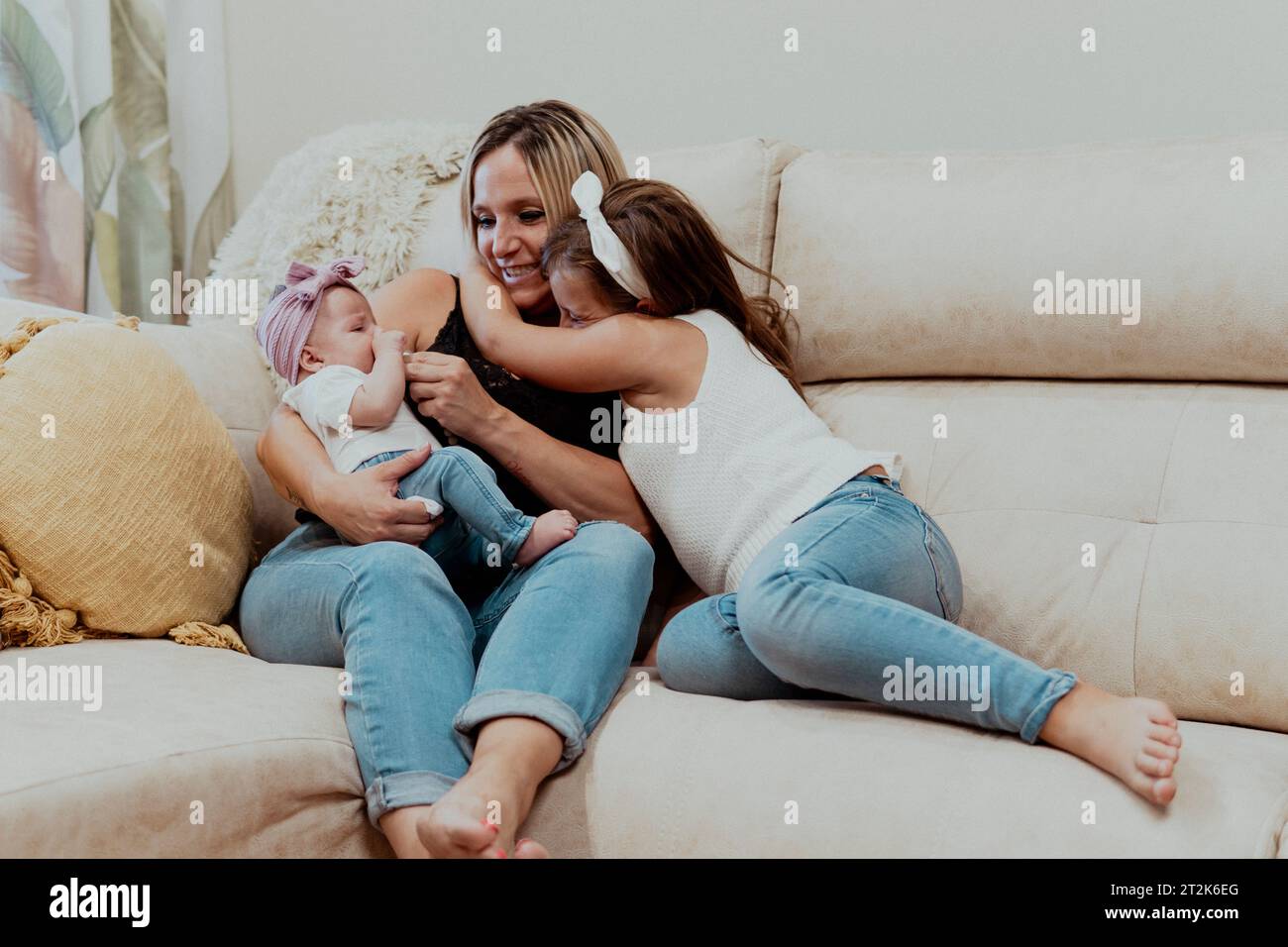 A young mother holding her baby while her toddler hug her Stock Photo