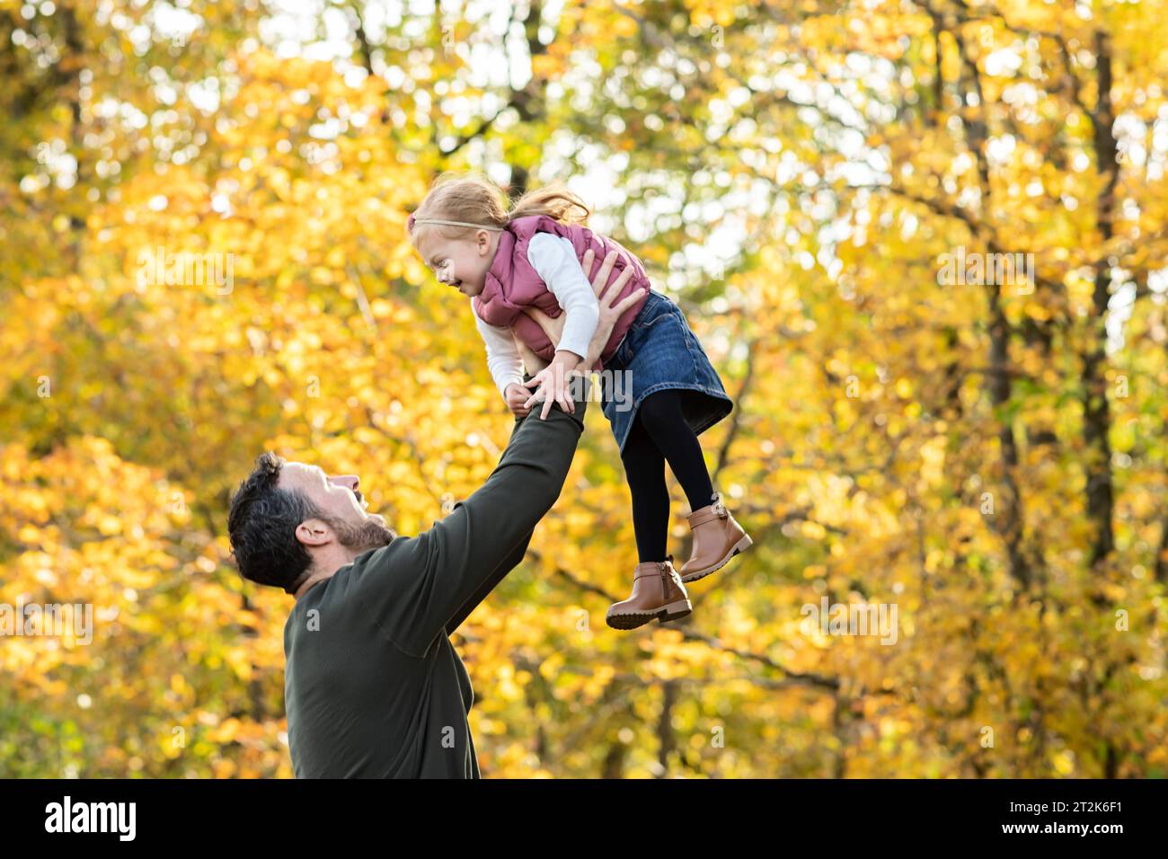 Dad lifting daughter in the air amidst a fall backdrop Stock Photo