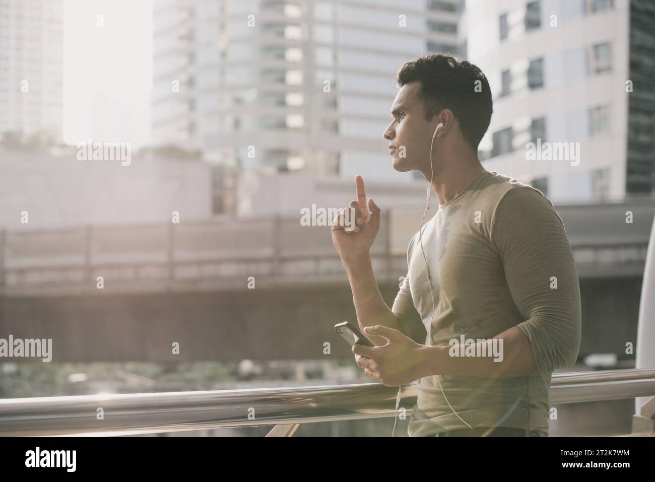 Young handsome Indian man wearing earphones listening to streaming music on smartphone in the city Stock Photo