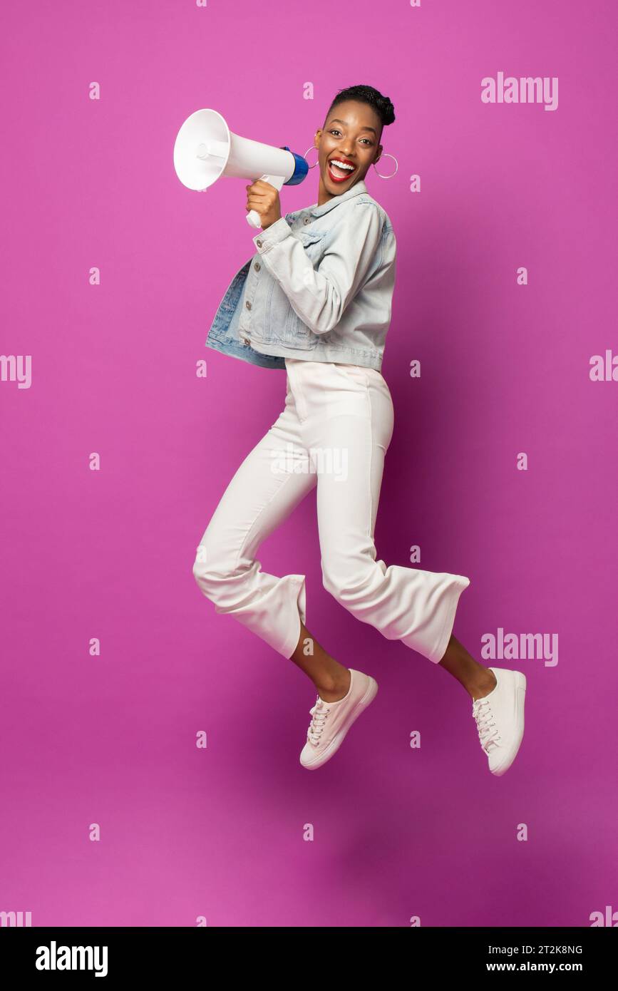 Energetic trendy young African American woman jumping with megaphone in ...