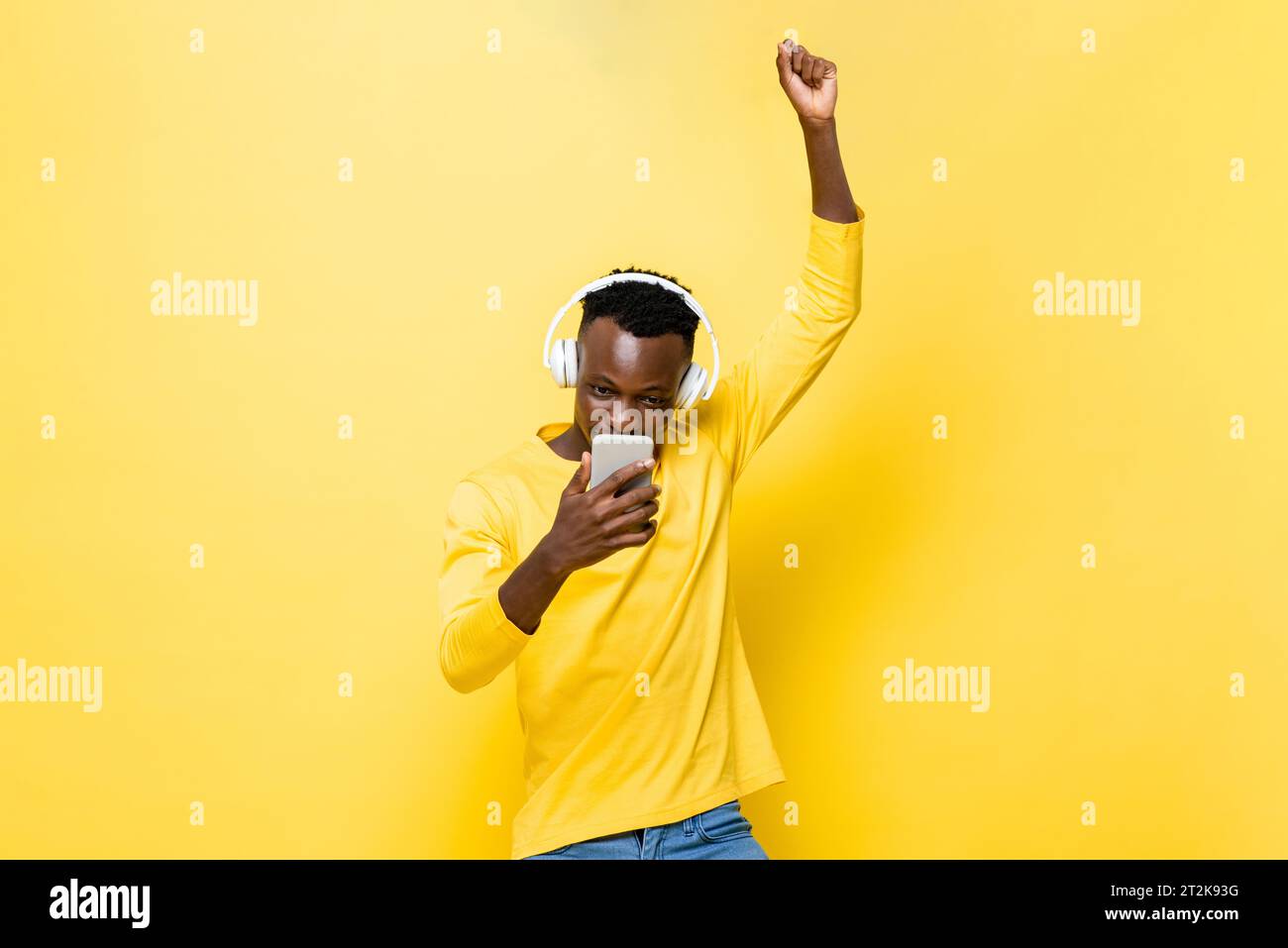 Young African man looking at mobile phone and raising hand up in studio yellow color isolated background Stock Photo