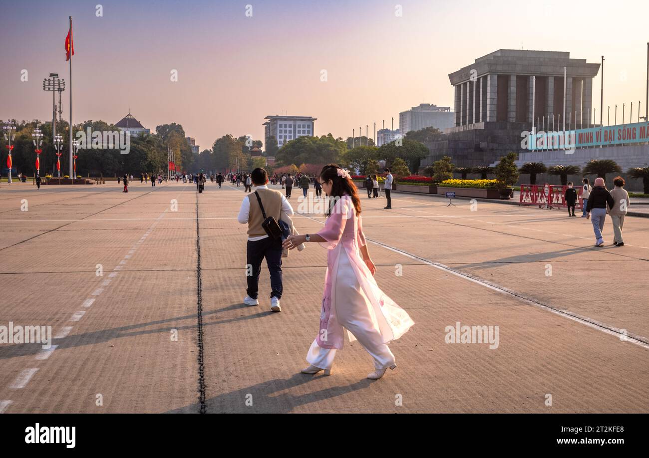 A Vietnamese woman in a traditional pink and white ao dai walks in Ba Dinh Square next to Ho Chi Minh's Mausoleum in central Hanoi, Vietnam. Stock Photo