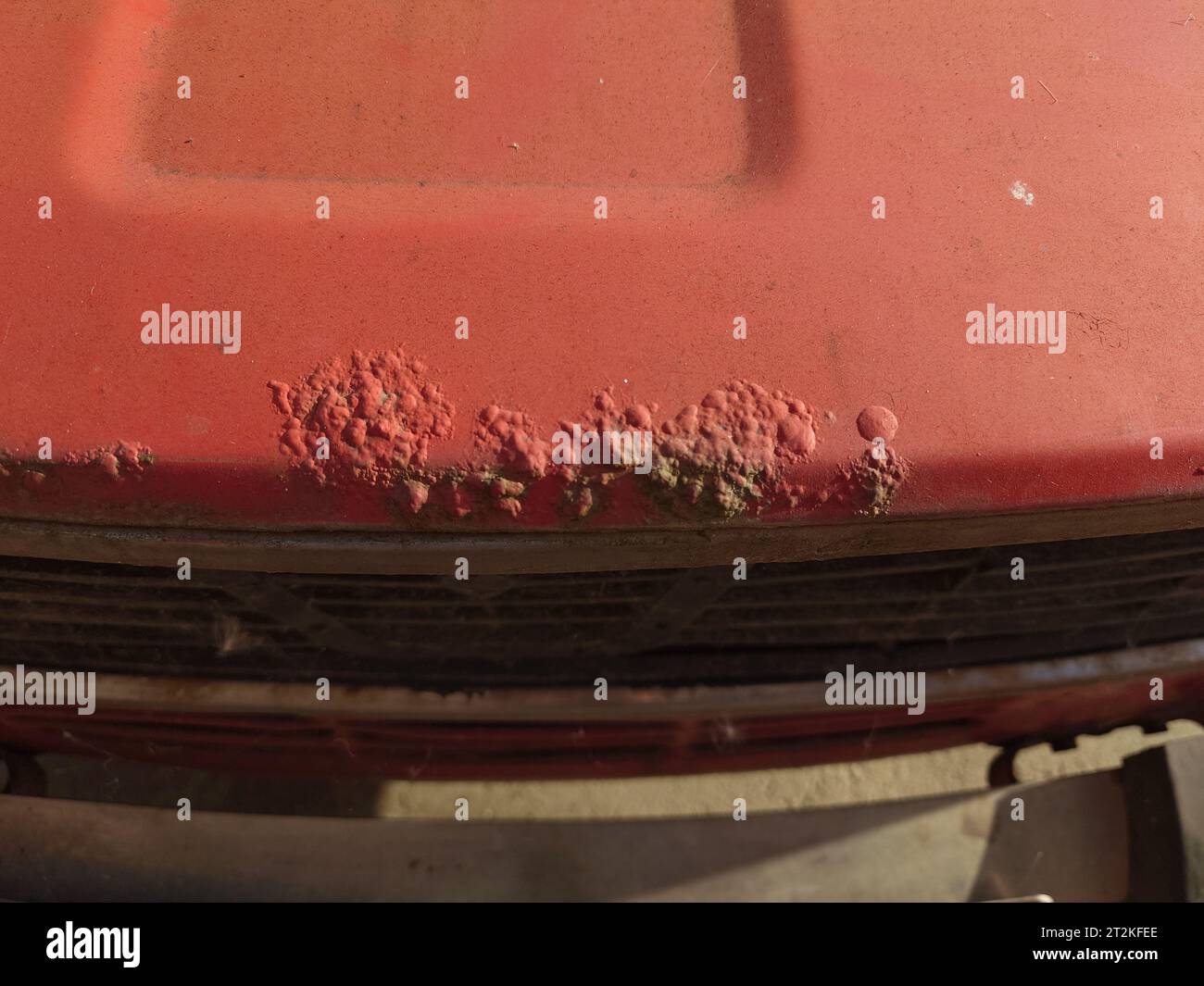 Rust bubbles under old red paint on an abandoned car's hood or