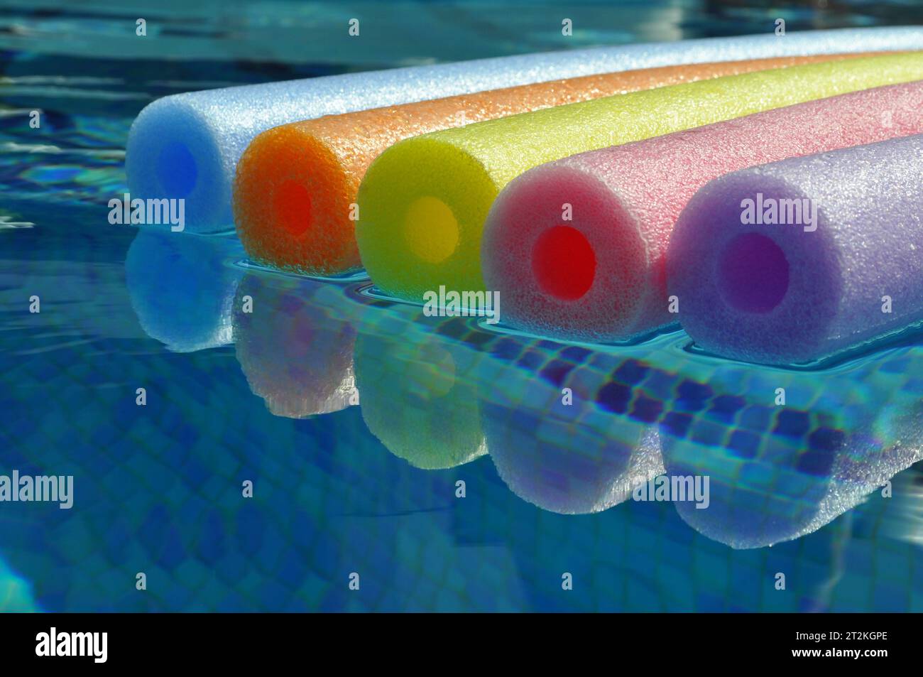 Rainbow coloured pool noodles floating in swimming pool, with reflection in water Stock Photo