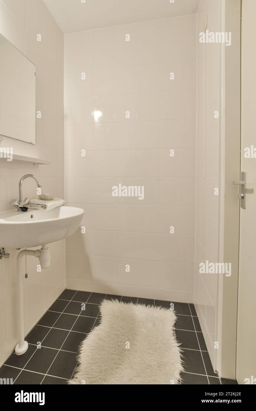 a small bathroom with black and white tiles on the floor next to a sink, mirror and toilet roller Stock Photo