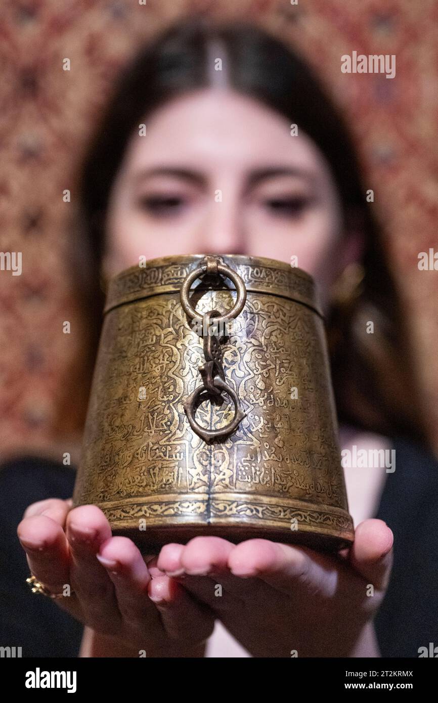 London, UK.  20 October 2023. A staff member with an 'inscribed bronze Zakat measure (mudd)', ordered by the Almohad Caliph Sultan Ya’qub al-Mansur ibn Yusuf, signed by Muhammad ibn Jafar, Spain or Morocco, dated 580 AH/1184 AD, (Est. £150,000 - 250,000), at a preview of upcoming sales of Arts of the Islamic World & India at Sothebys.  The auction takes place at Sothebys New Bond Street galleries on 25 October 2023.  Credit: Stephen Chung / Alamy Live News Stock Photo