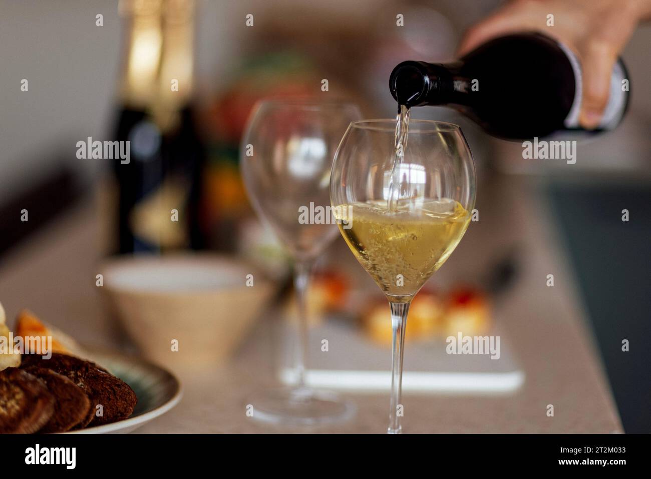 Close-up of an elegant glass with a long stem with champagne. The process of pouring sparkling wine into a goblet. Bottles of wine, plates with snacks Stock Photo