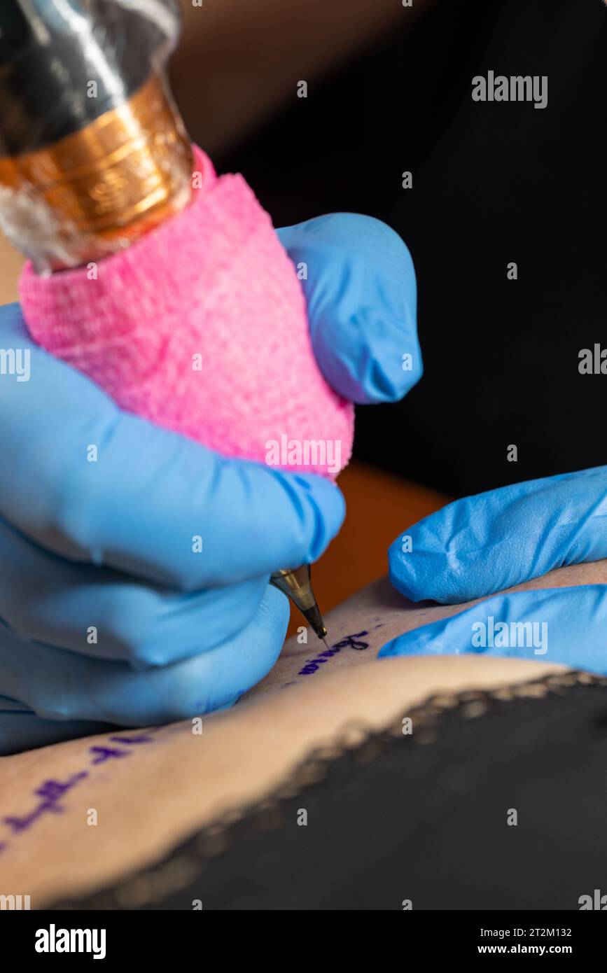Cropped close up of a female tattoo artist working at his studio tattooing a string of text on the collarbone of her female client. Woman getting tattooed by professional tattooist. High quality photo Stock Photo