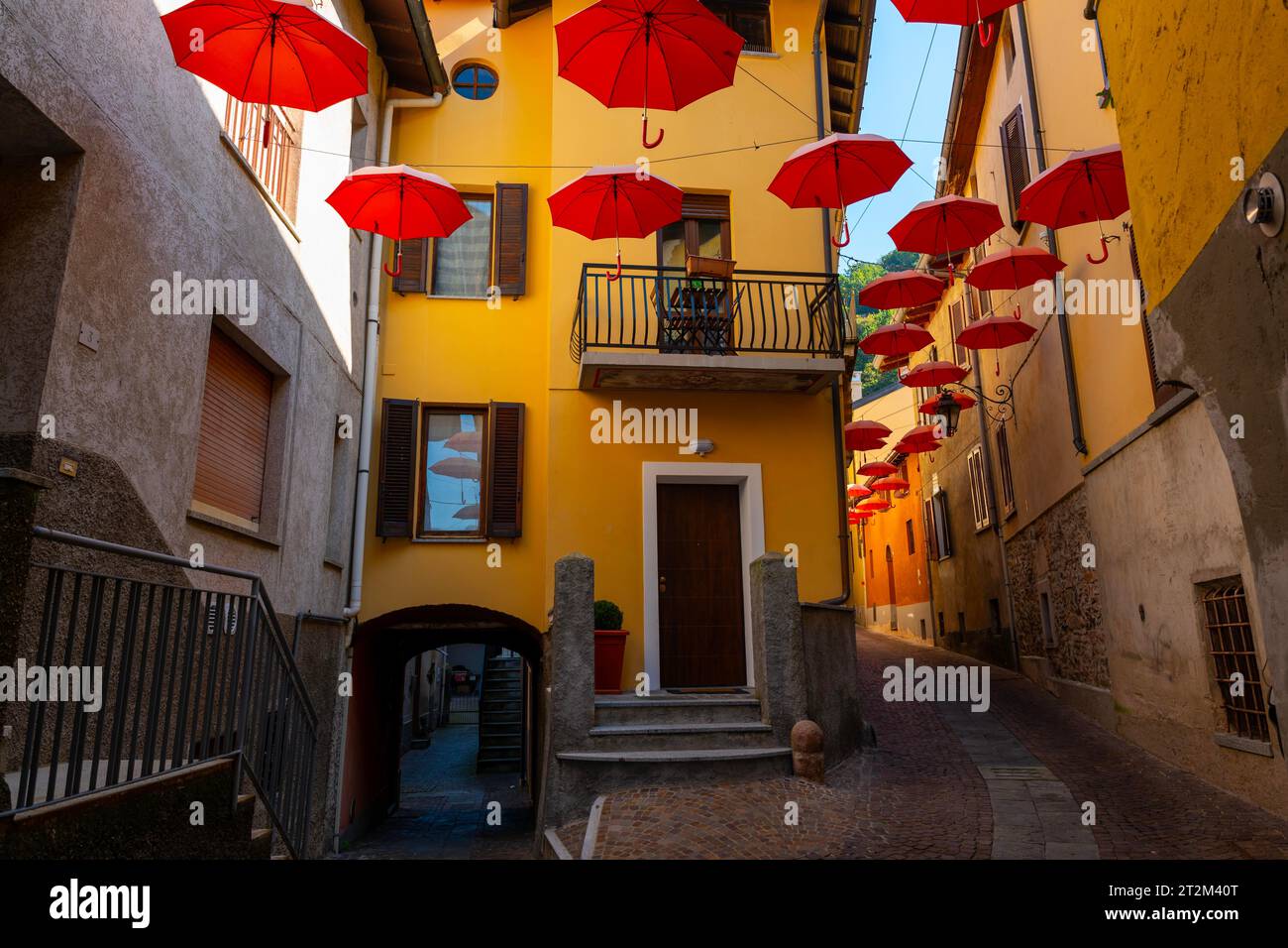 City Street in Porto Ceresio with Hanging Umbrellas in a Sunny Summer Day in Porto Ceresio, Lombardy, Italy Stock Photo