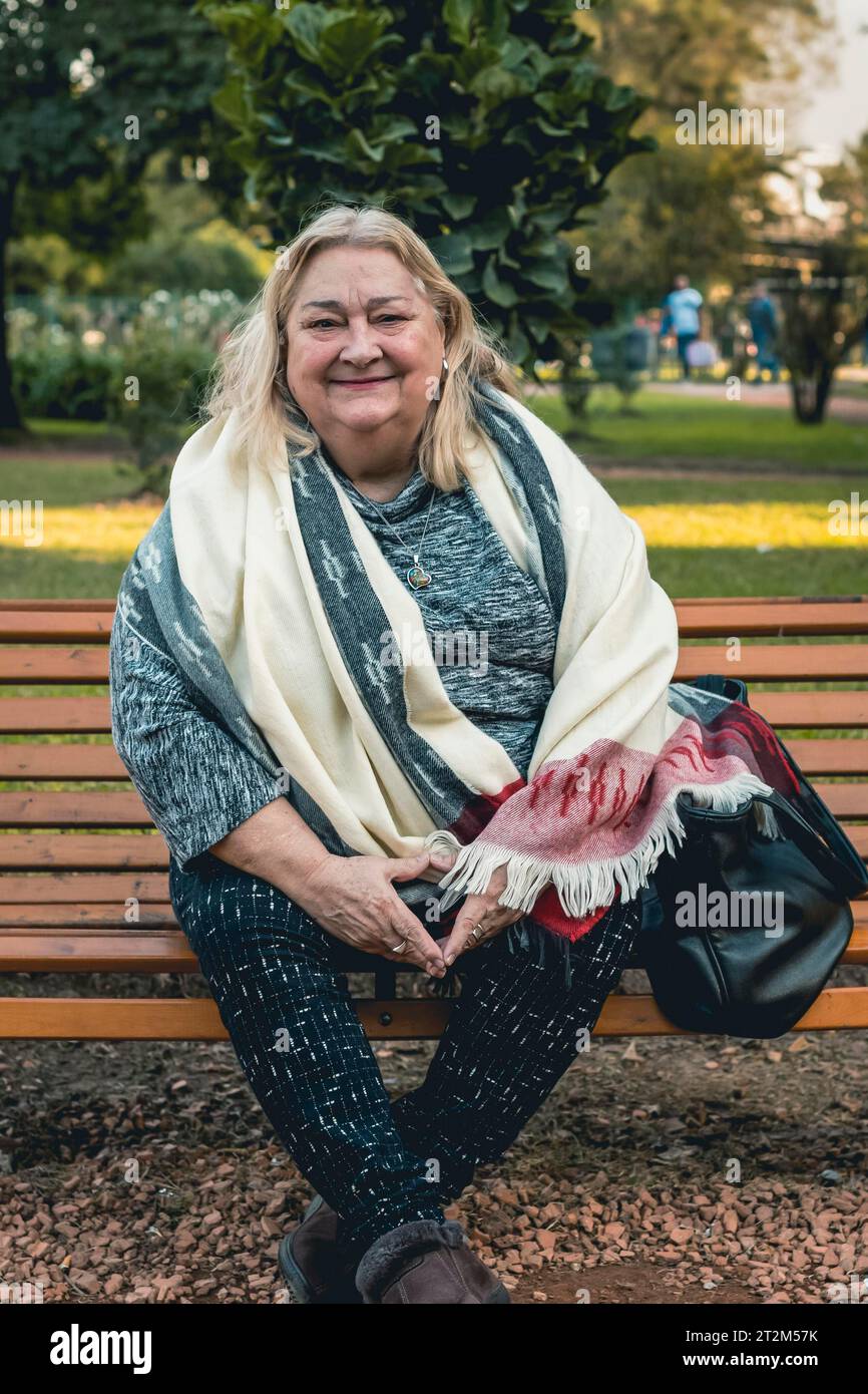 Portrait of a cheerful senior woman relaxing outdoors, sitting on a bench at a public park Stock Photo