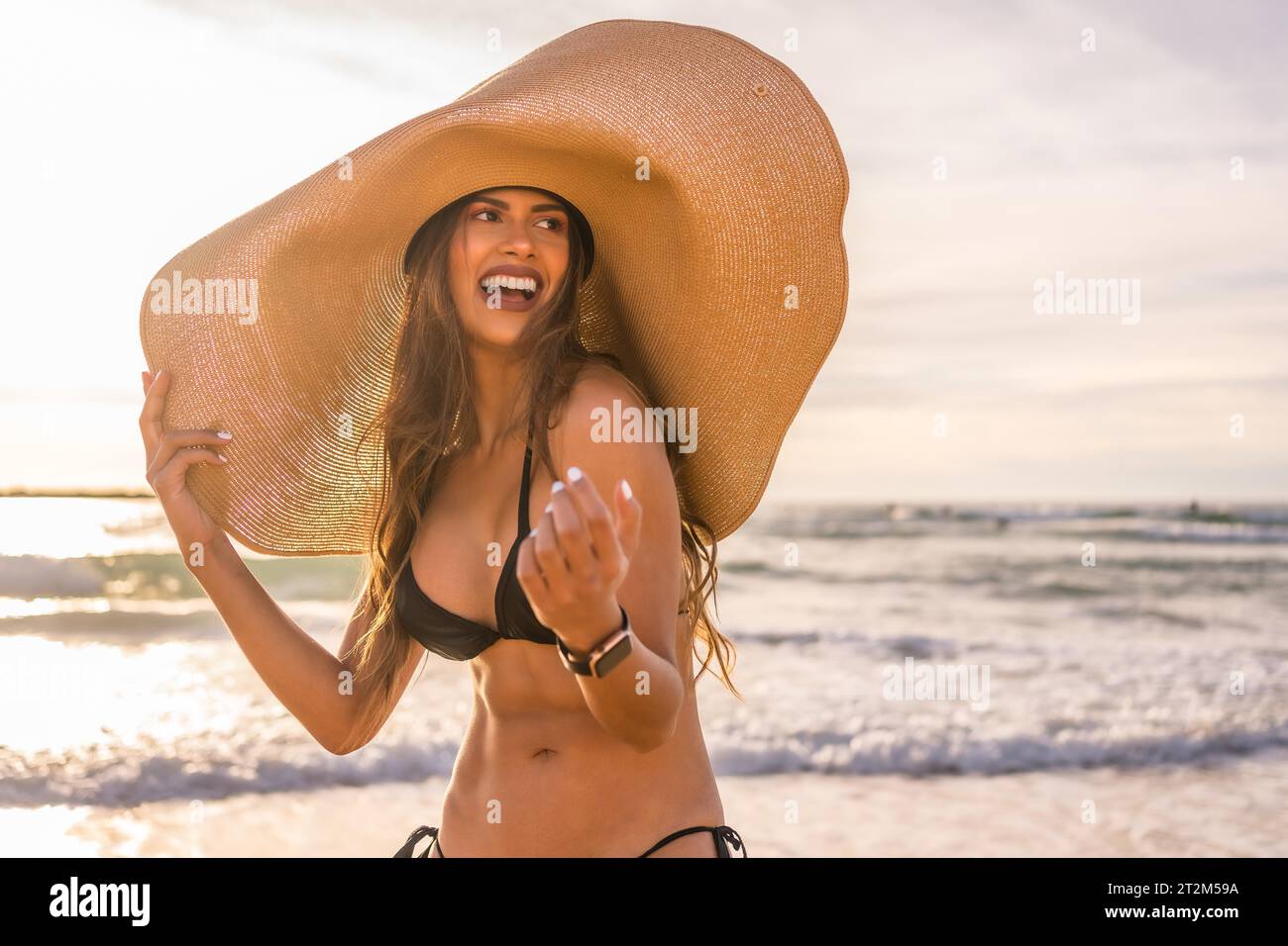Happy young woman wearing sunhat on beach during sunset Stock Photo