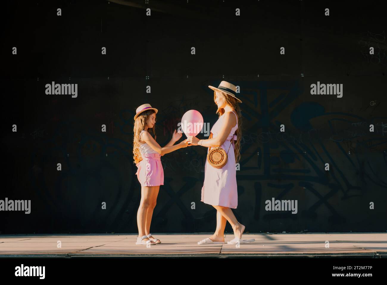 mother and daughter stand in pink dresses with flowing long hair on a ...
