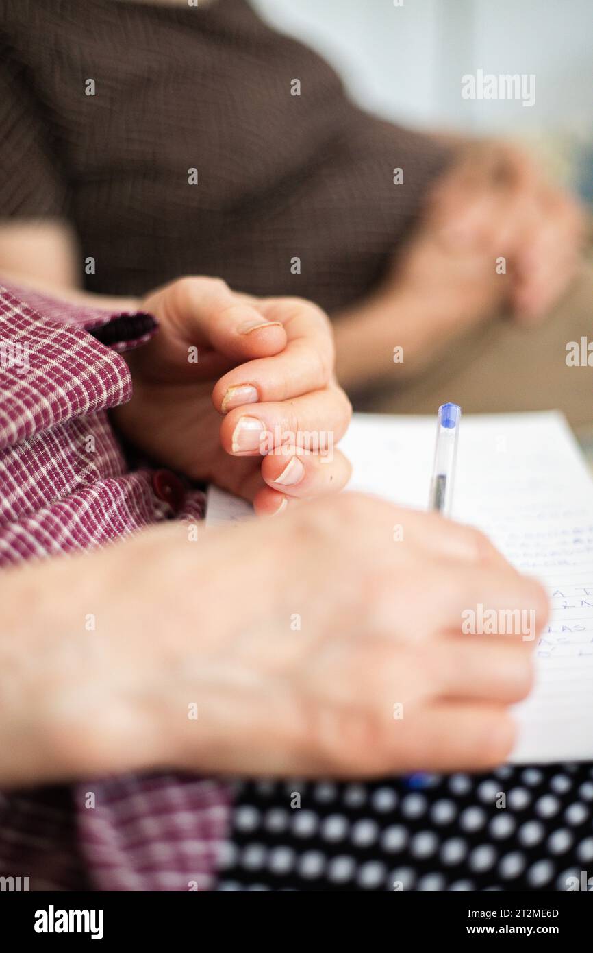 Close up of a woman holding a pen. Two elderly people sitting on the sofa relaxed and with their hands on their stomachs in the form of a rest. Stock Photo