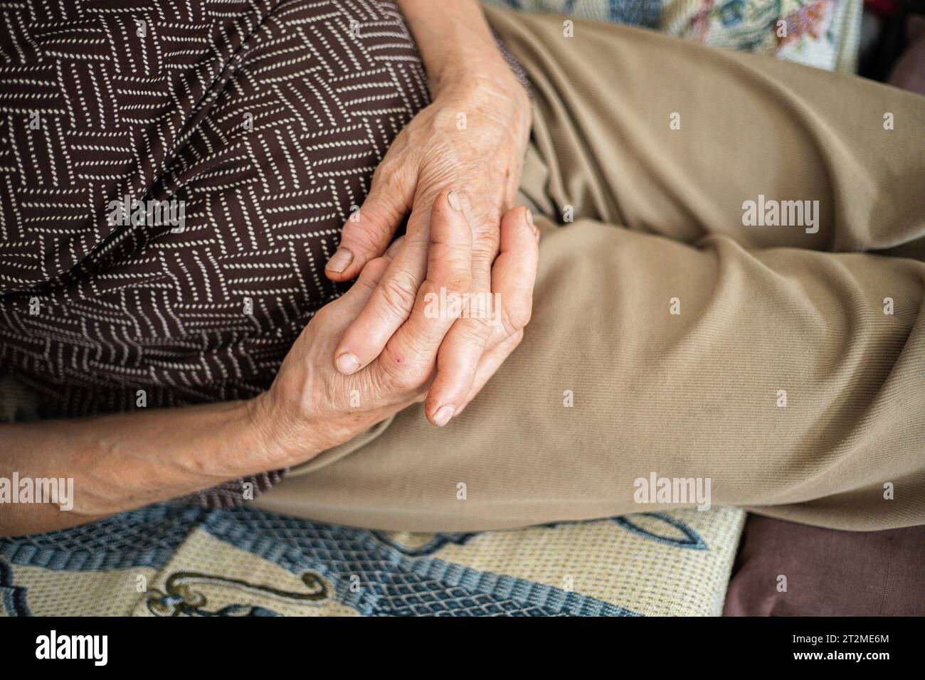 Hands of the elderly person. Highlight of senior woman's hands on her belly in the form of rest. Moment of relaxation on the sofa, nap break. Close up Stock Photo