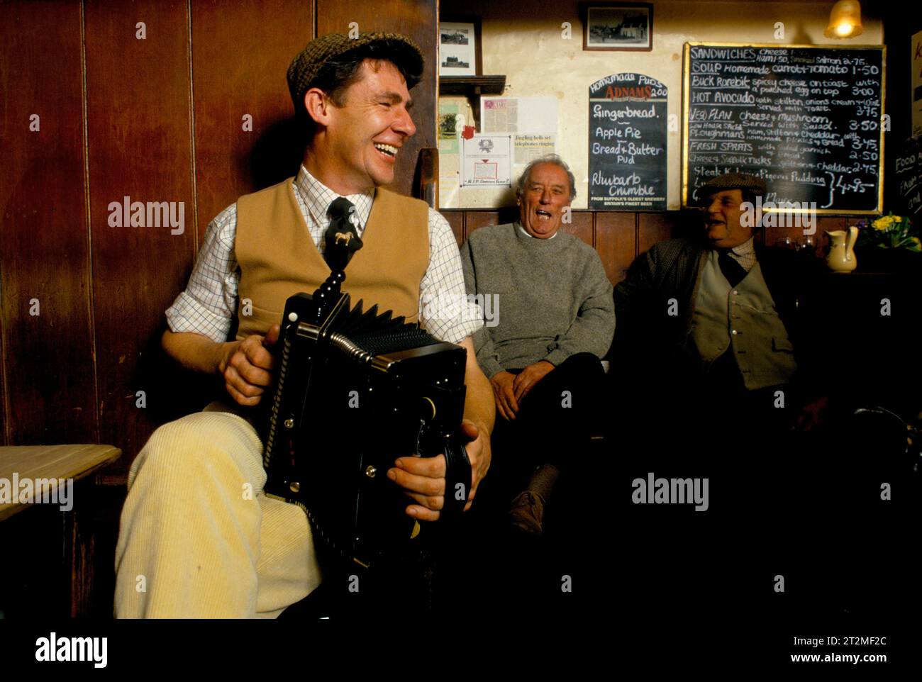 Traditional folk music UK 1980s. Farmers and countrymen gather at the Kings Head, and also know as the Low House pub, in  Laxfield. Traditional story telling, reciting of poetry and folk music songs are performed in an informal manner every Sunday morning. A local farmer playing a melodeon. Laxfield, Suffolk, England  1985. 1980s HOMER SYKES Stock Photo