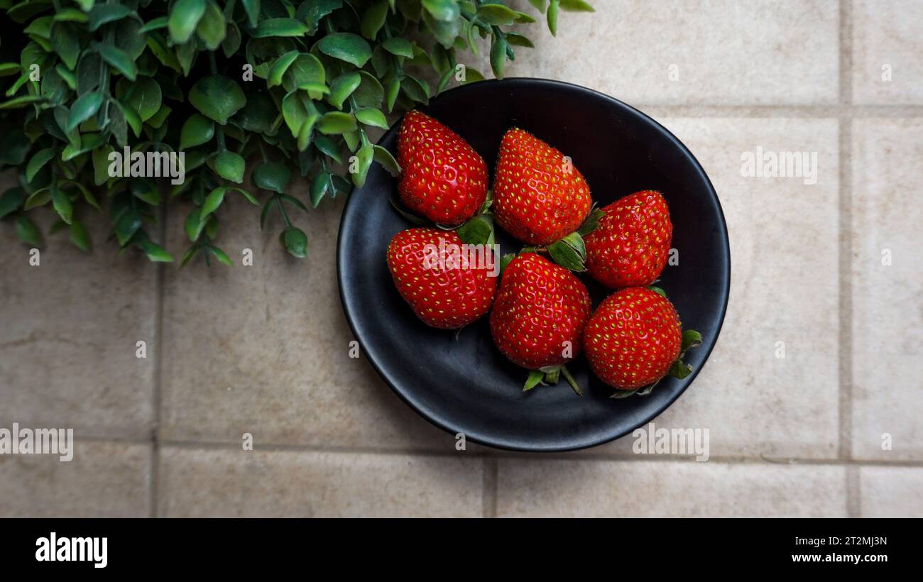 Strawberries are arranged on a black plate with green leaves decorated on the side Stock Photo