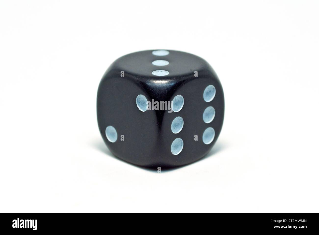 Close up of a black die or dice with bluish coloured spots, isolated