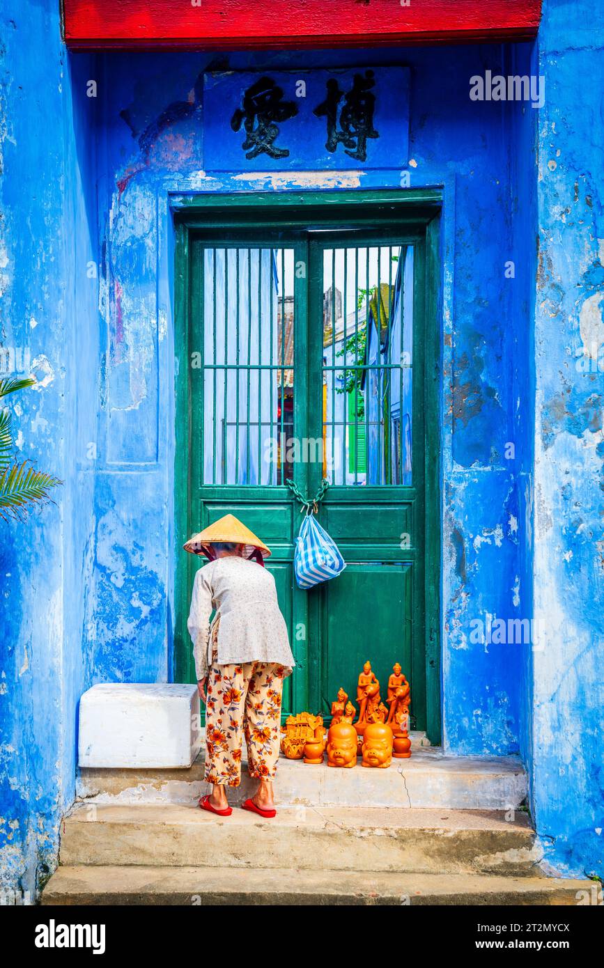 Hoy An, Vietnam, November 20, 2022: An elderly lady is setting up a display of hand-crafted statues on the steps of a temple in Hoy An, Vietnam Stock Photo