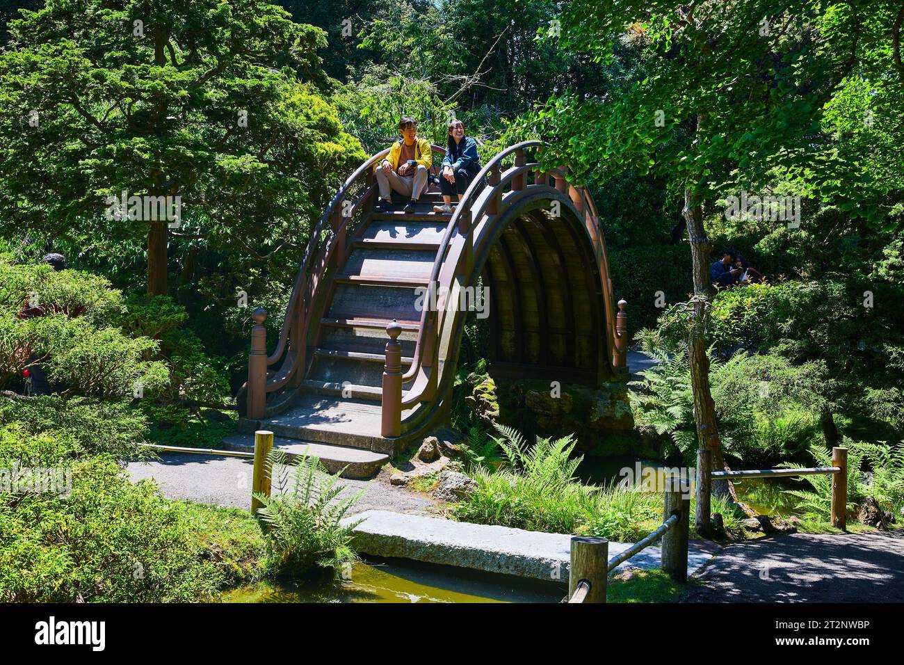 Man and a woman smiling and sitting on top of a curved bridge in Japanese Tea Garden Stock Photo