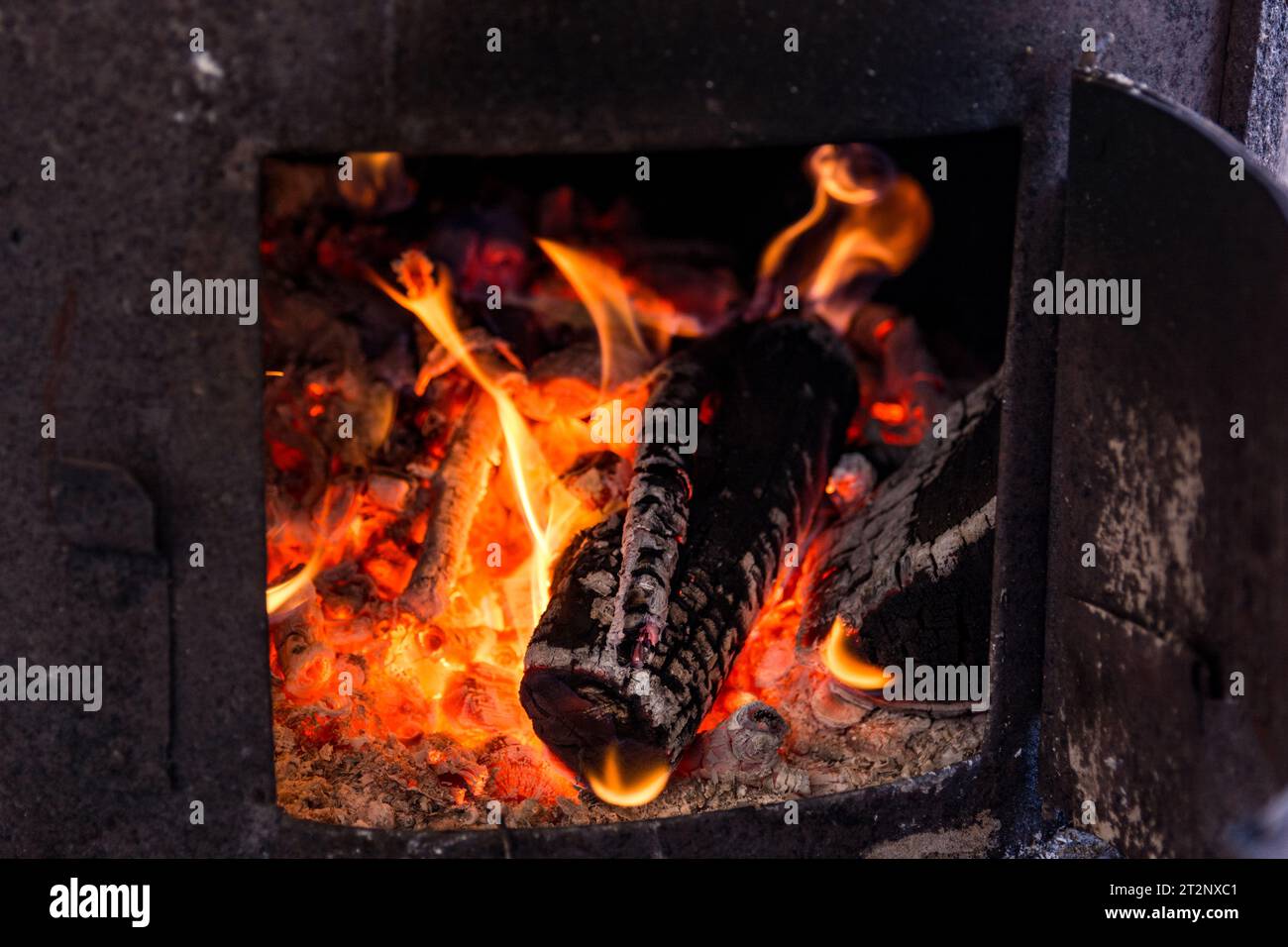 A close up of burning wood in an old stove. The wood is charred and surrounded by red embers and flames Stock Photo