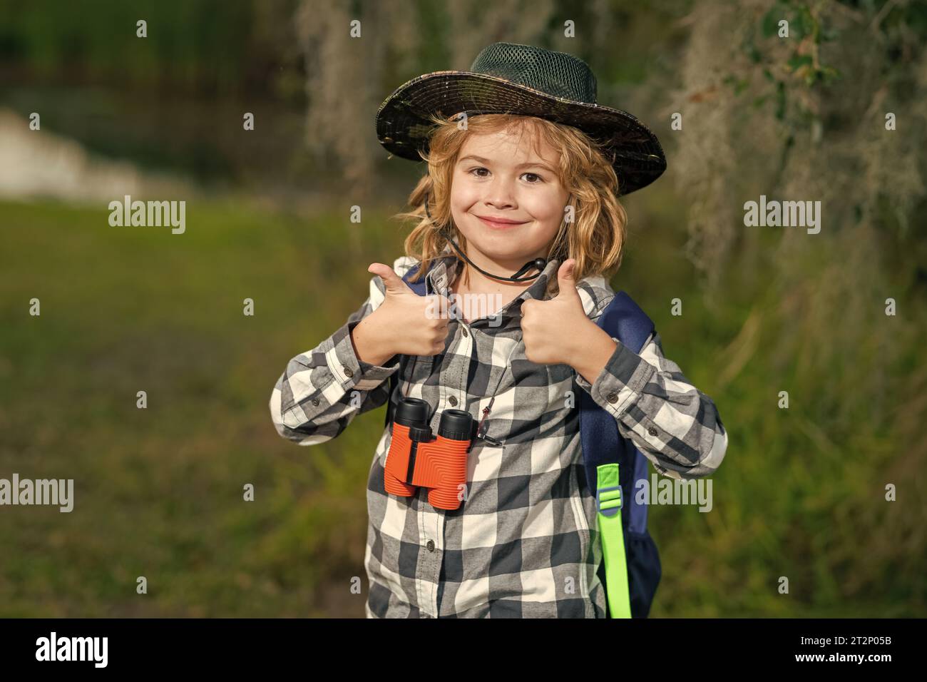 Child with binoculars travelling outdoors. Boy traveler with backpack in a summer day. Portrait of a little boy exploring wildlife. Hiking and adventu Stock Photo