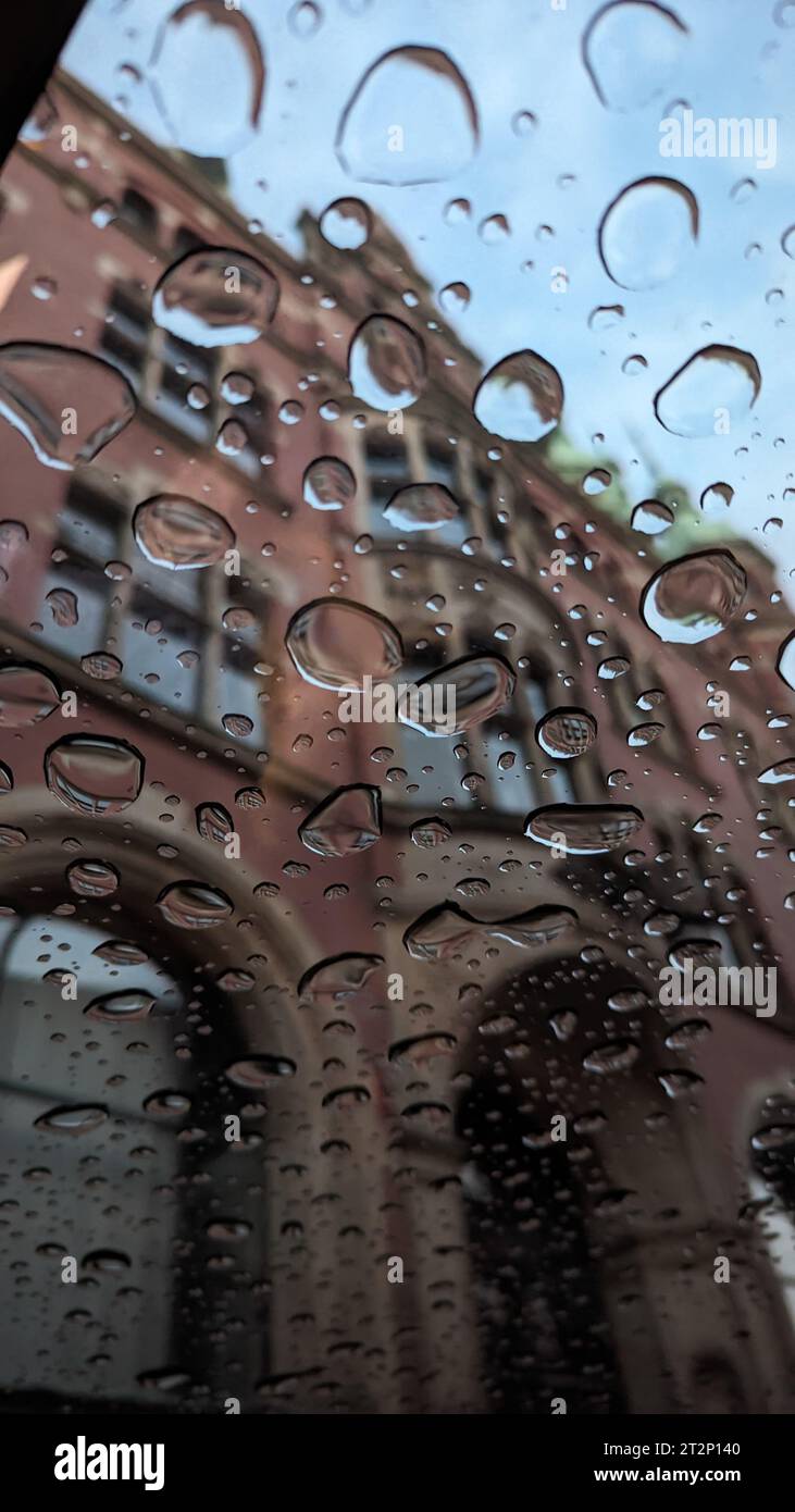 A closeup of the raindrops on the car window with a building in the ...