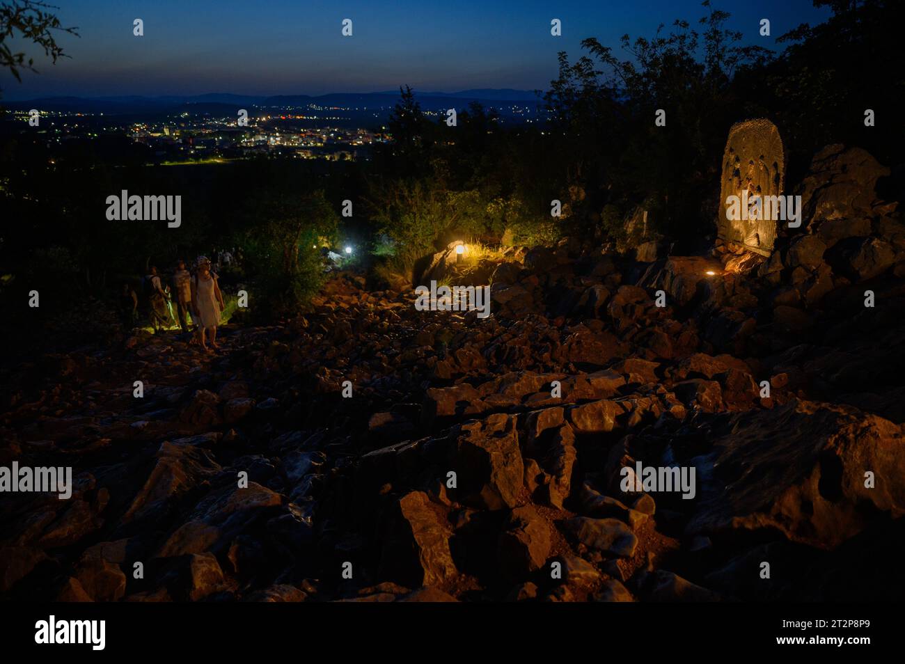 Mount Podbrdo in Medjugorje at night. People are ascending and praying the rosary. The sculpture: Fourth Joyful Mystery – The Presentation of Jesus. Stock Photo
