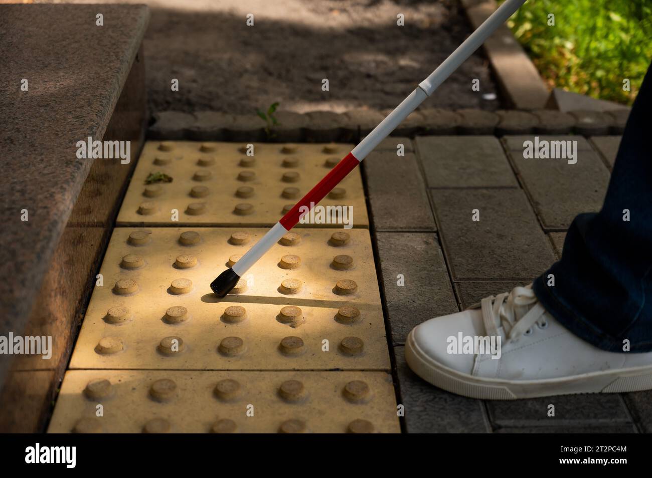 Close-up of female foot, walking stick and tactile tiles. Blind woman climbing stairs using a cane.  Stock Photo