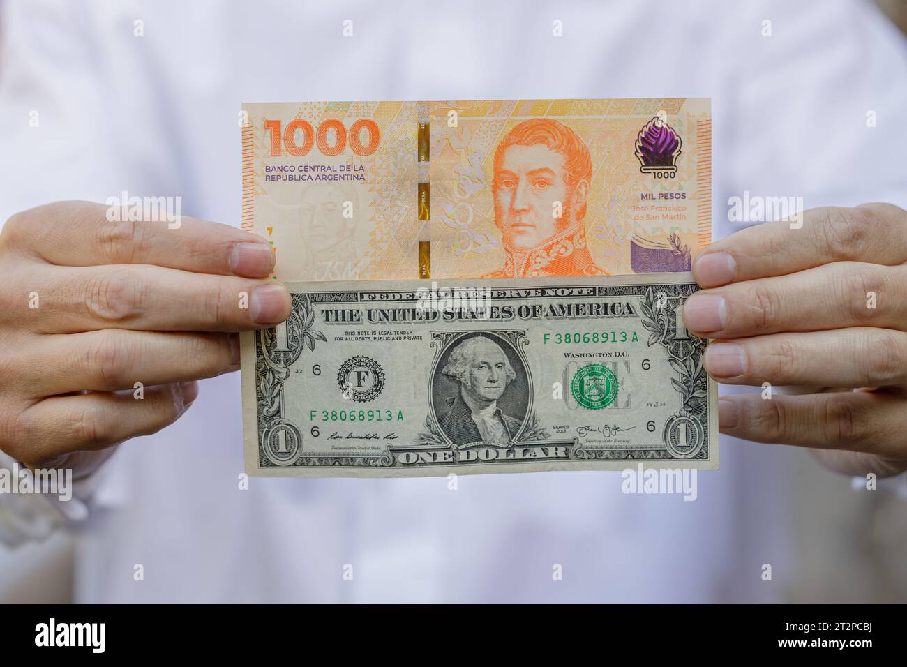 Close-up of a man's hands holding a one-dollar bill next to a thousand Argentine peso bill. Stock Photo