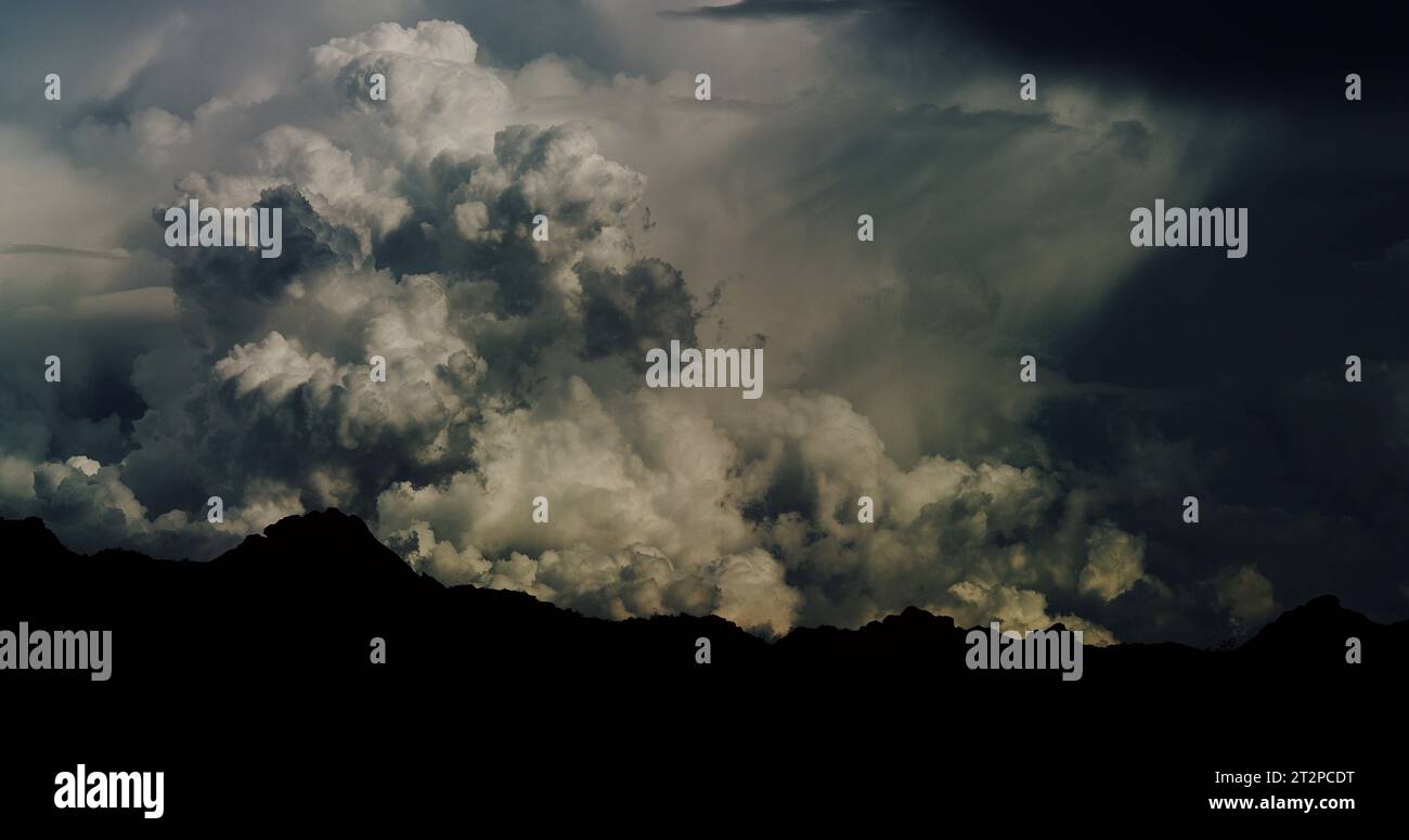 Chaotic and wildly billowing cumulonimbus cloudscape and a developing monsoon storm event over a silhouetted mountain range. Stock Photo