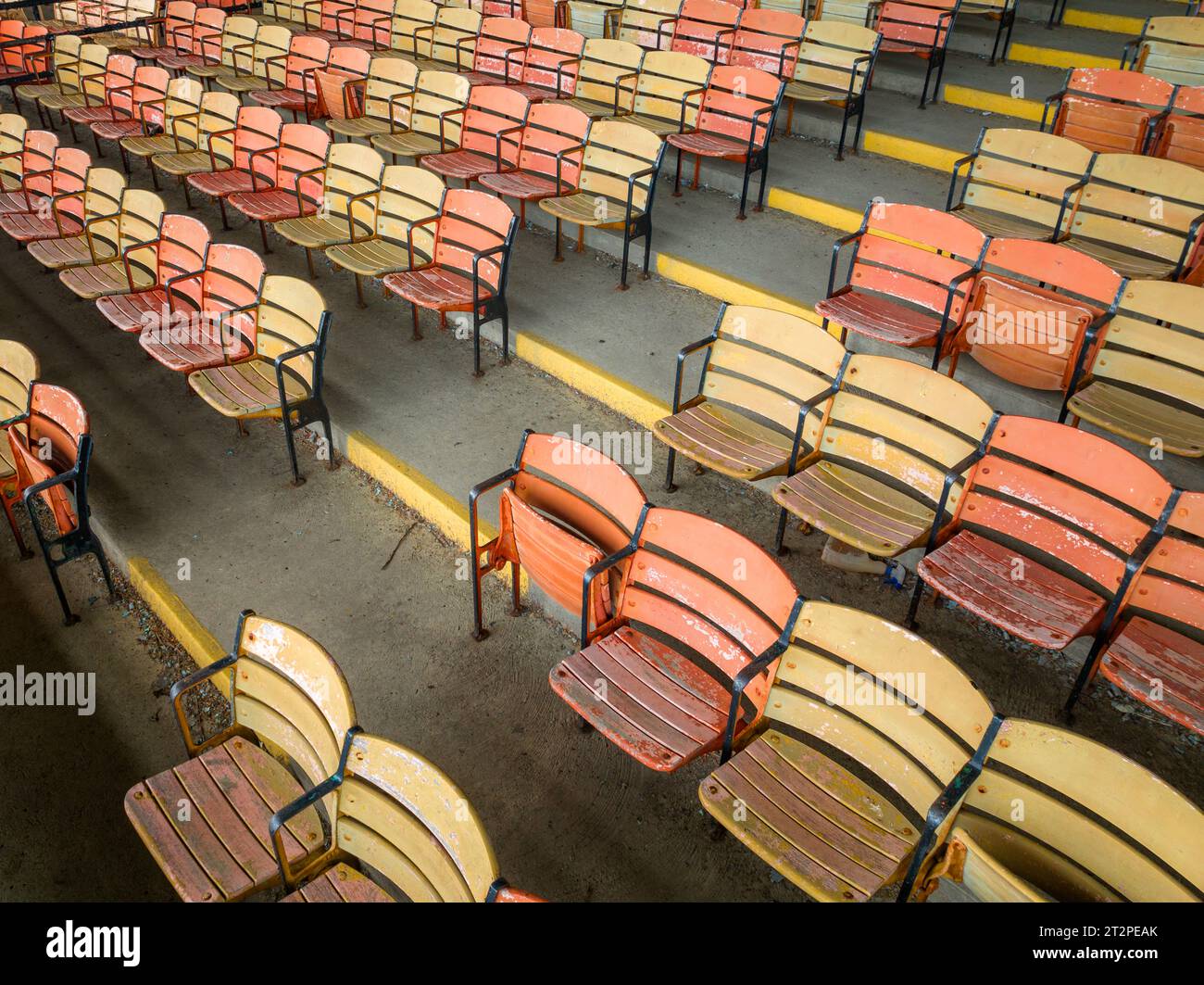 Old faded orange and yellow painted wooden seats at a abandoned a stadium grandstand. Stock Photo