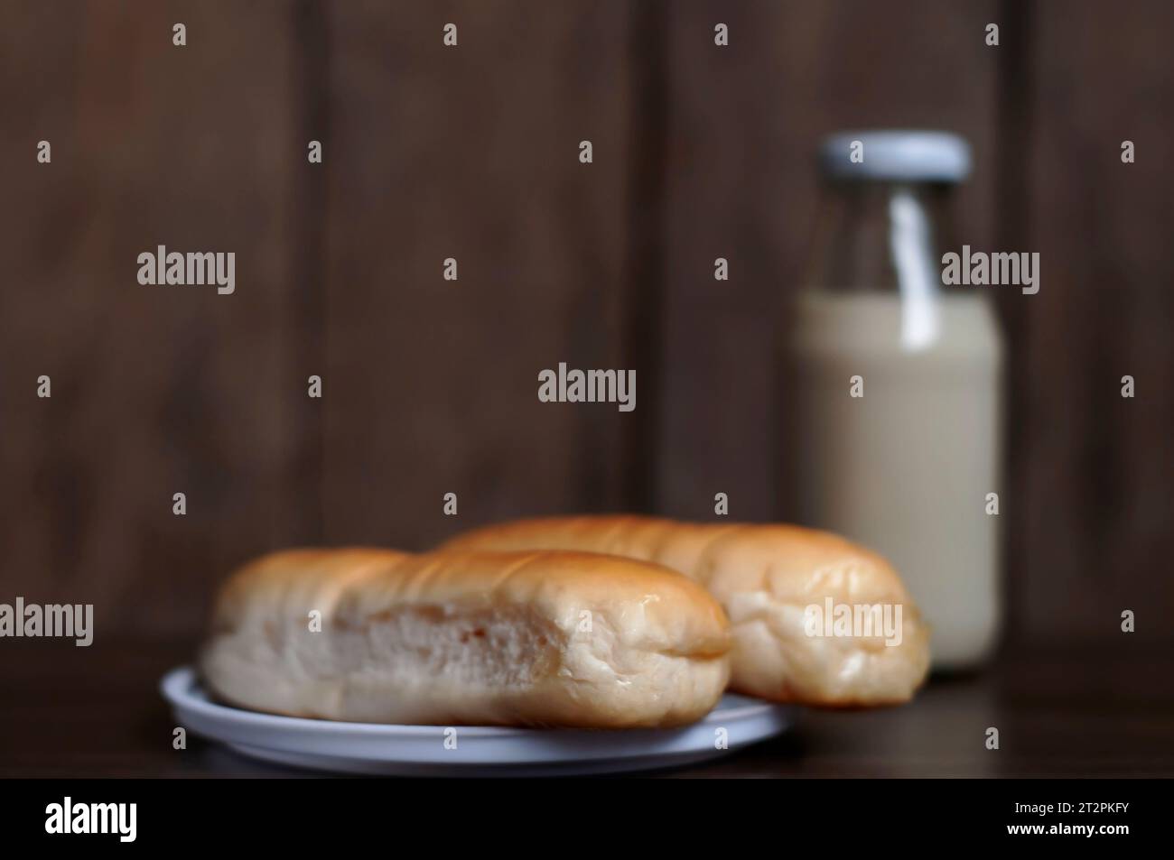 Bread on a white plate sits on a wooden board table with milk in a bottle behind it with copy space. Blurred background Stock Photo