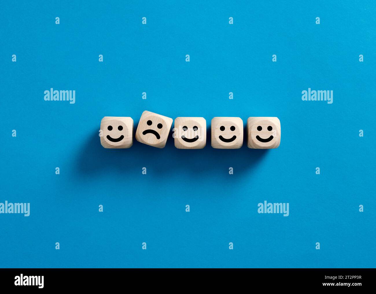 Unhappy member of the team. Teamwork adaptation. Work stress. Social nonconformity. One unhappy face between happy faces on wooden cubes. Stock Photo