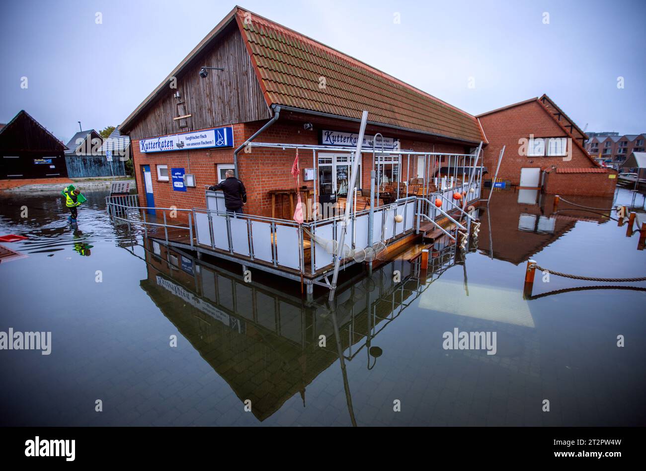 Wismar, Germany. 21st Oct, 2023. Buildings in the fishing port are in the water after the storm surge on the Baltic Sea coast. The cleanup work begins in the morning. In Wismar, the water level remained below 1.60 meters in the night of 21.10.2023 and dropped to less than 1.50 meters by early morning. Credit: Jens Büttner/dpa/Alamy Live News Stock Photo