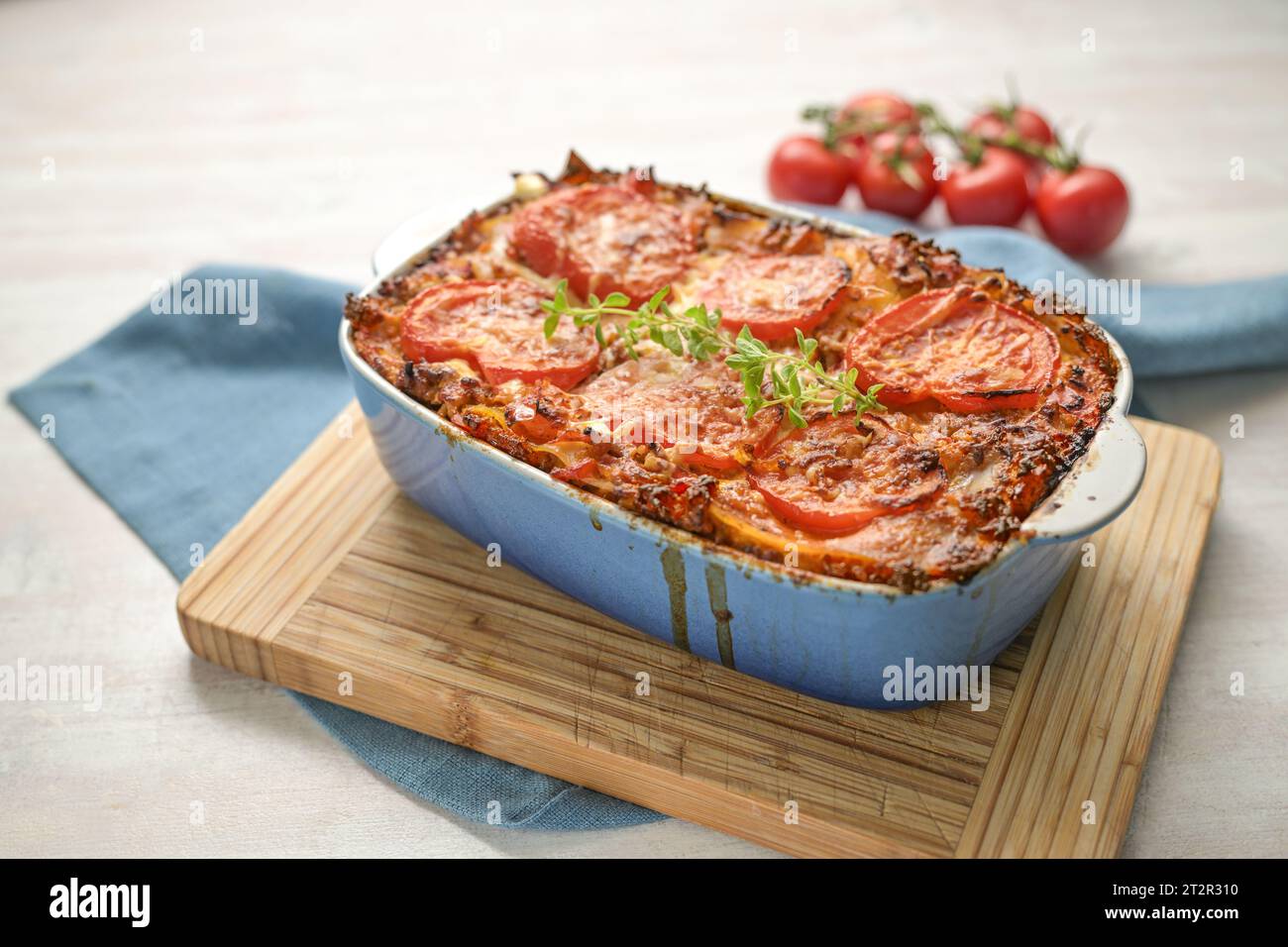 Lasagna, fresh from the oven, casserole dish of flat pasta sheets, ground beef sauce, vegetables and tomatoes, topped with melted cheese on a wooden k Stock Photo