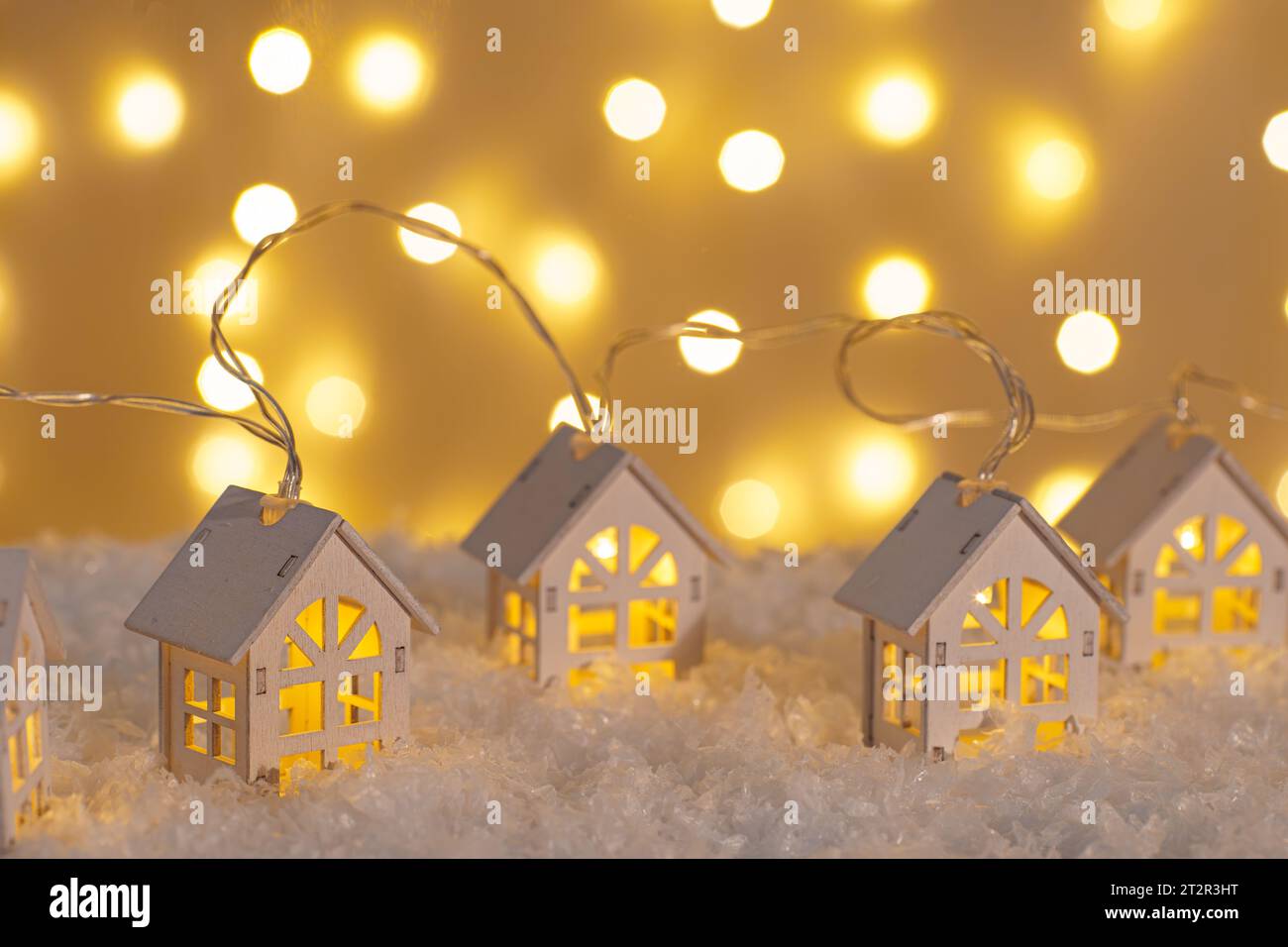 Wooden houses garland string lights on snow and glowing lights bokeh background. Christmas, New Year greeting card with copy space. Holiday illuminati Stock Photo