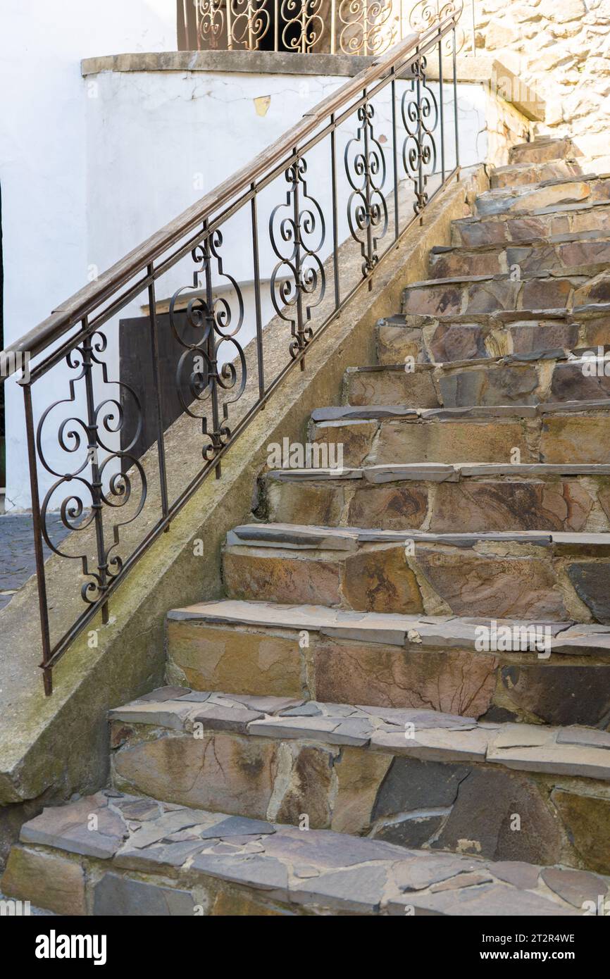 Brown stairs with black patterned iron railings. Way up to old stone ...